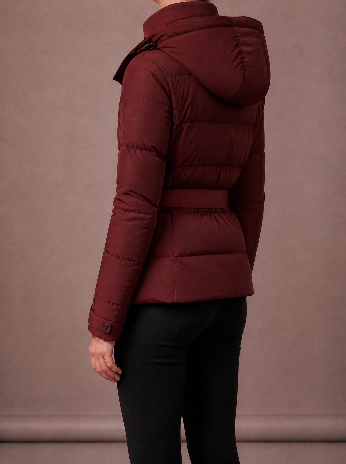 Burgundy belted winter jacket from the side and back, showing hood and quilting, studio view