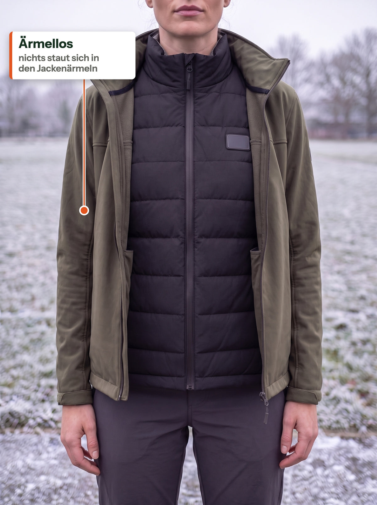 Schwarze Heizweste unter einer offenen olivgrünen Softshelljacke auf einem frostigen Feld: ärmellos, nichts staut sich in den Jackenärmeln