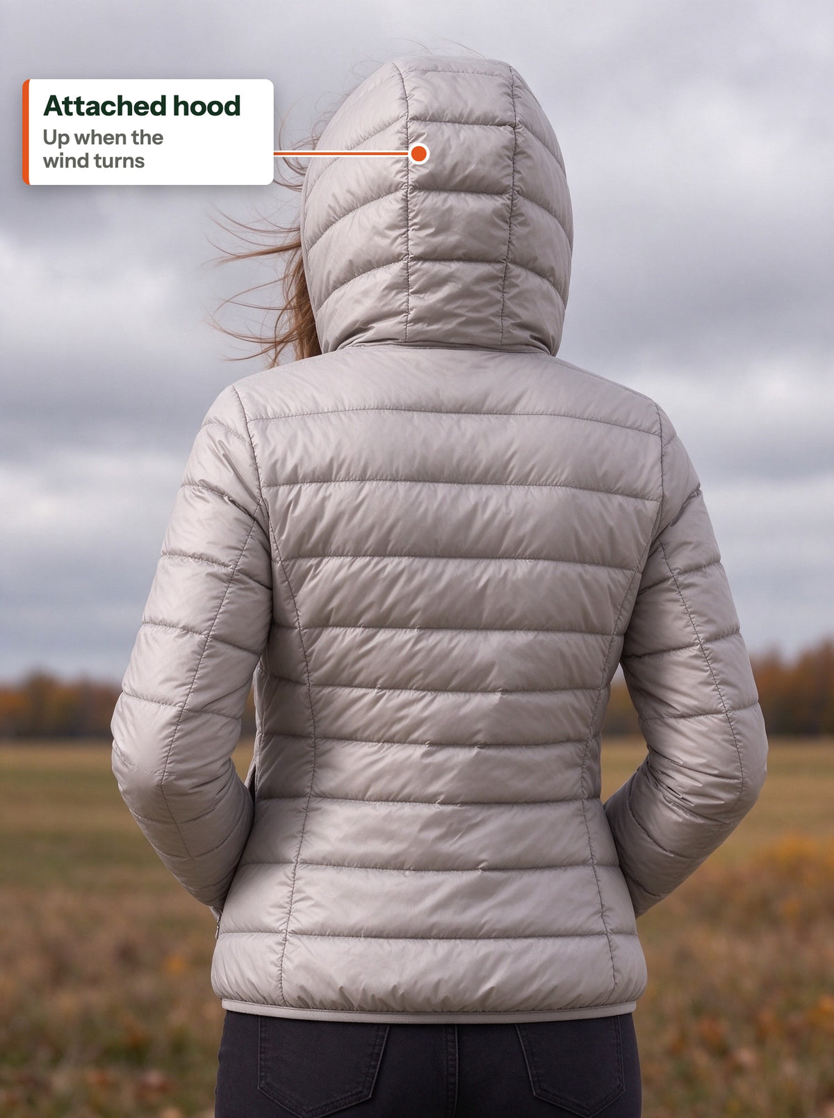 Back view of the grey light down jacket with the hood up on a windy field (EN label)