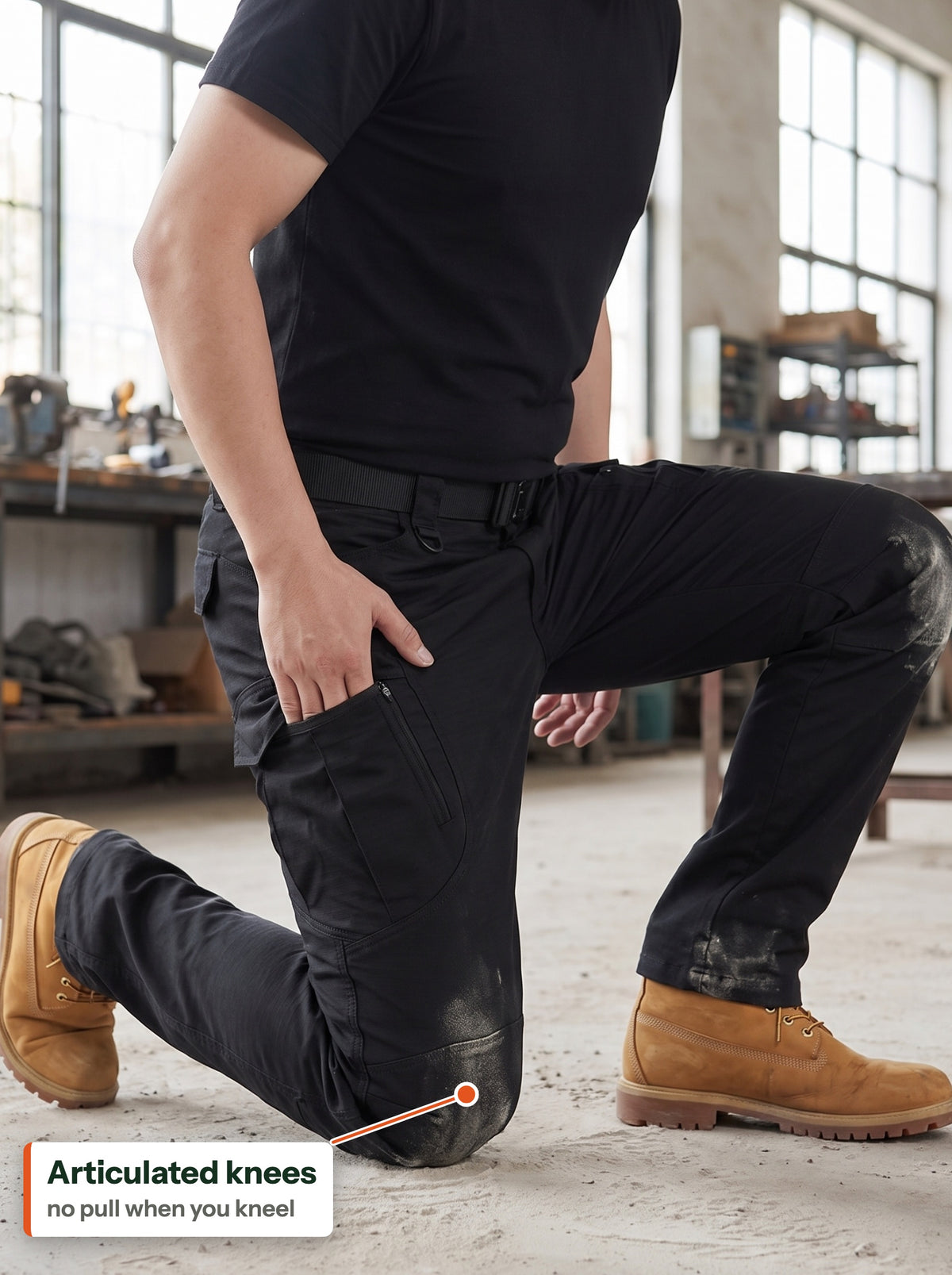 Articulated knees: black tactical cargo trousers kneeling on concrete in a workshop (EN label)