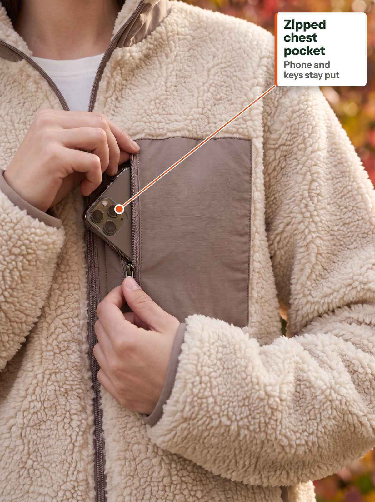 Phone going into the zipped woven chest pocket of the beige teddy jacket (EN label)