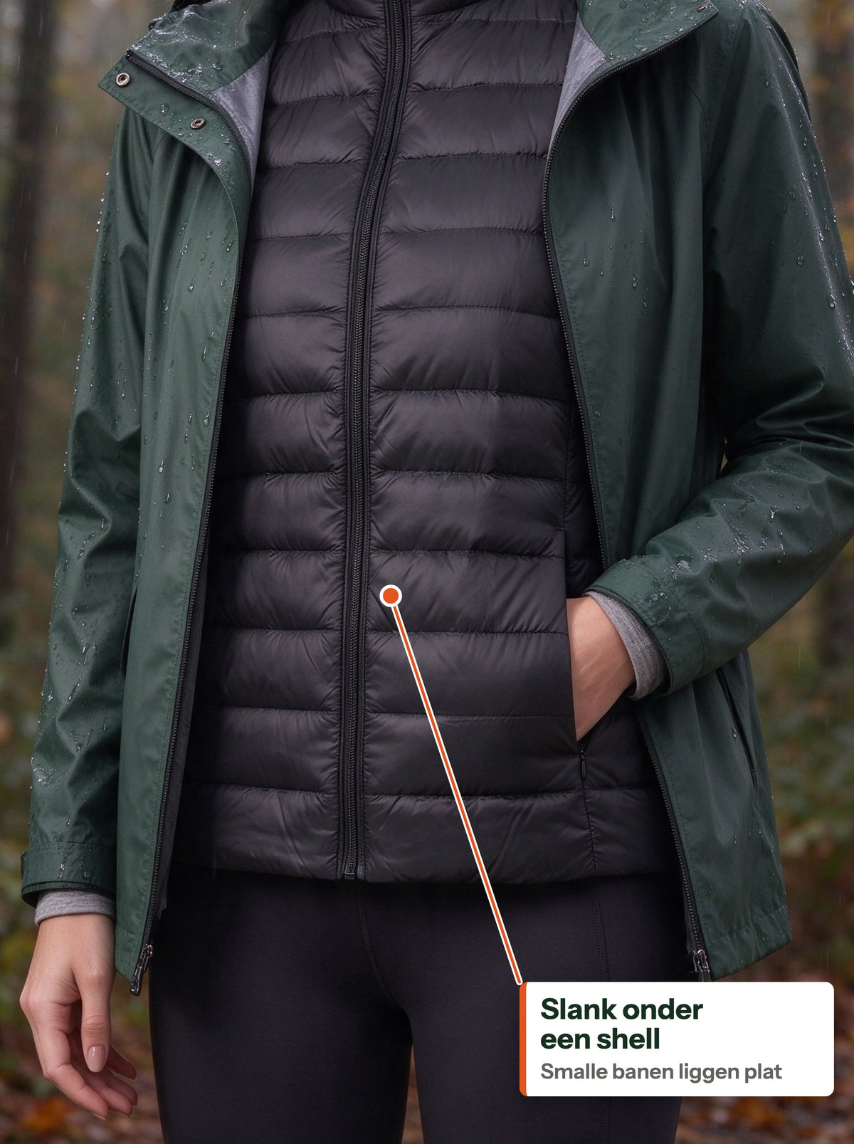 Black down vest worn under an open green rain shell in the forest (NL label)