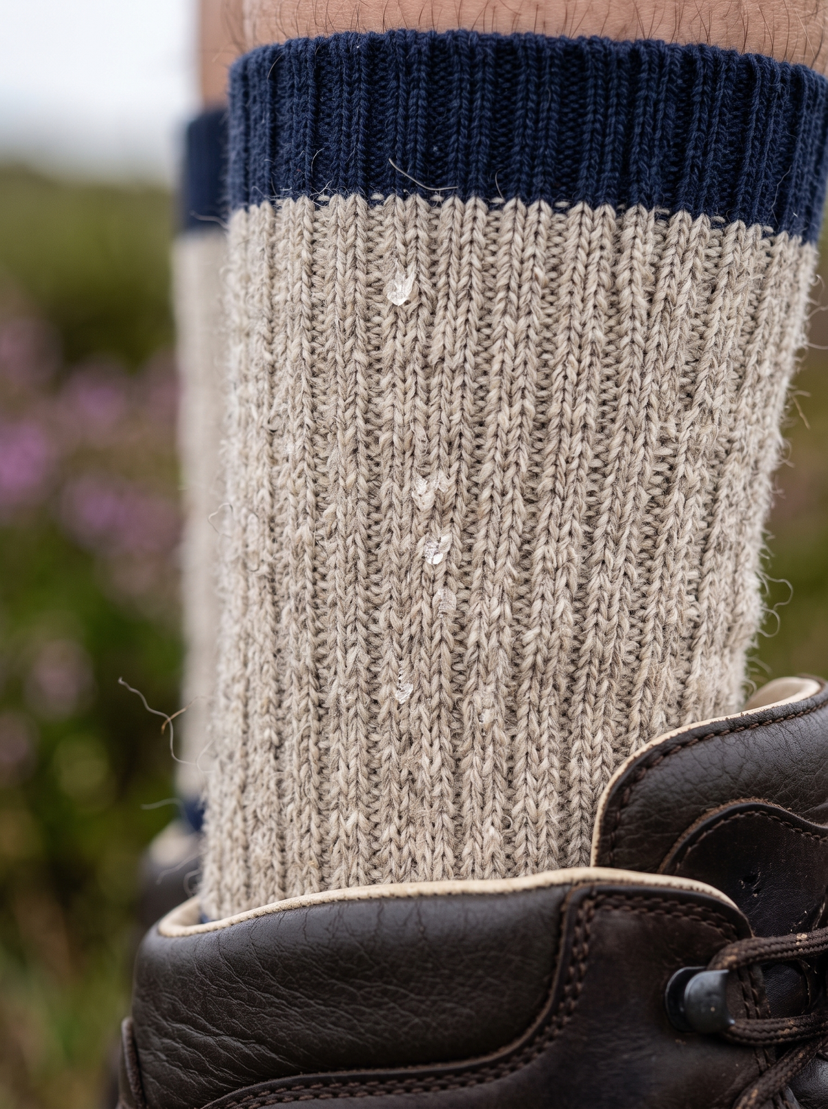 Thick oatmeal wool crew sock with a navy cuff above a leather walking boot, drizzle droplets on the knit