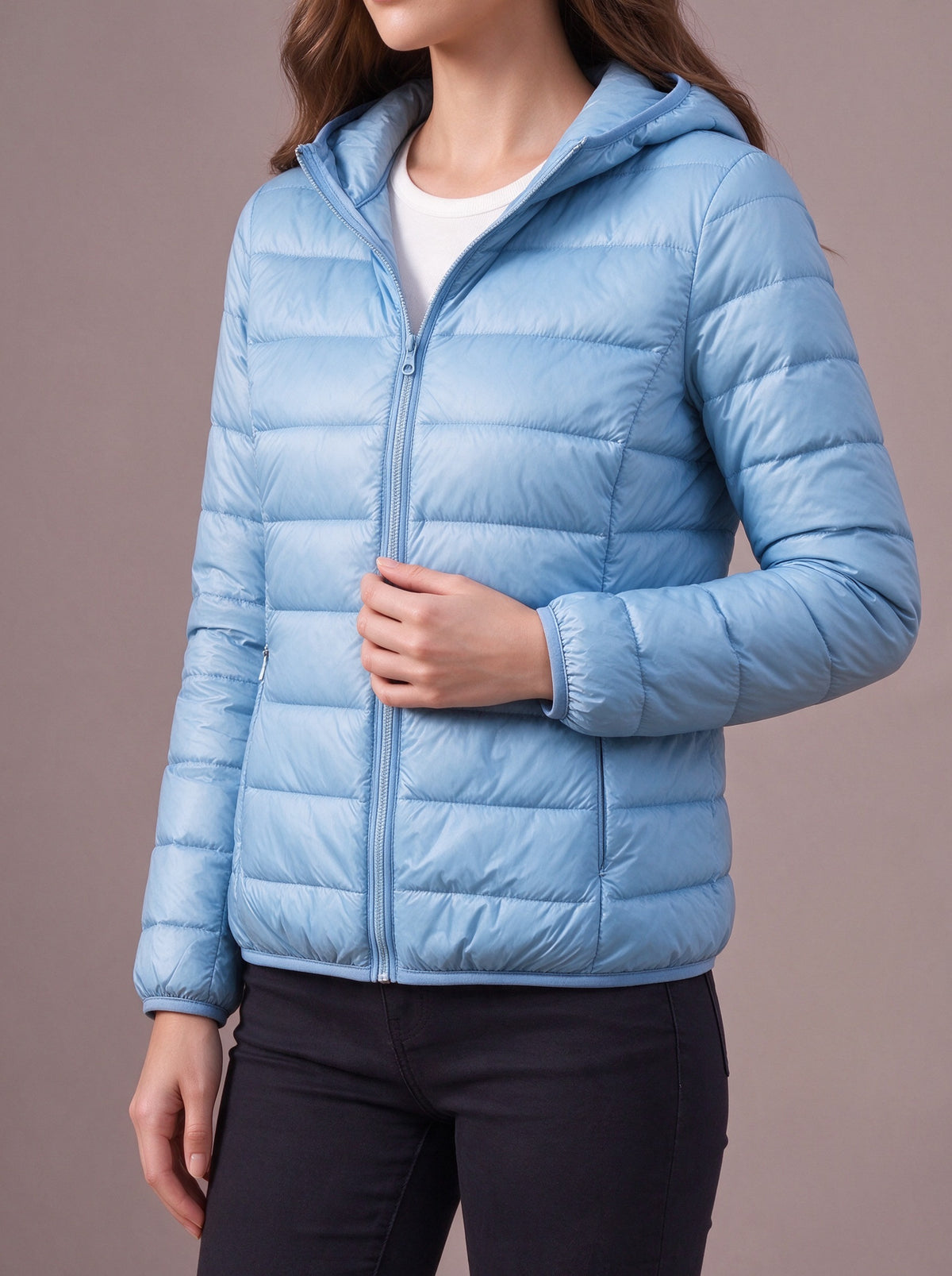 Light blue light down jacket with attached hood, hand on the zip, studio view