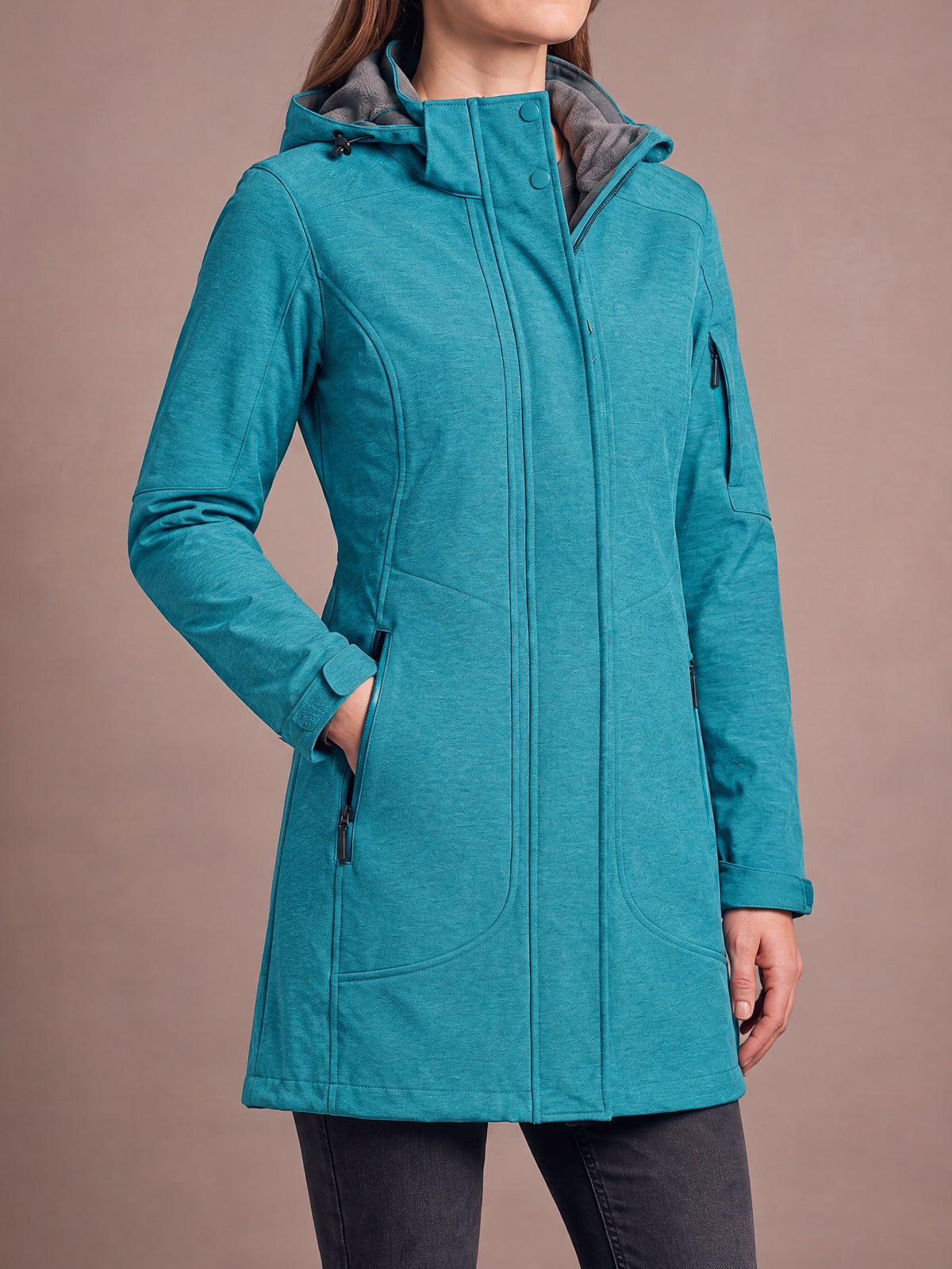 Long fleece-lined softshell coat in turquoise teal worn with a hand in the zipped hand pocket, snap collar and grey fleece-lined hood