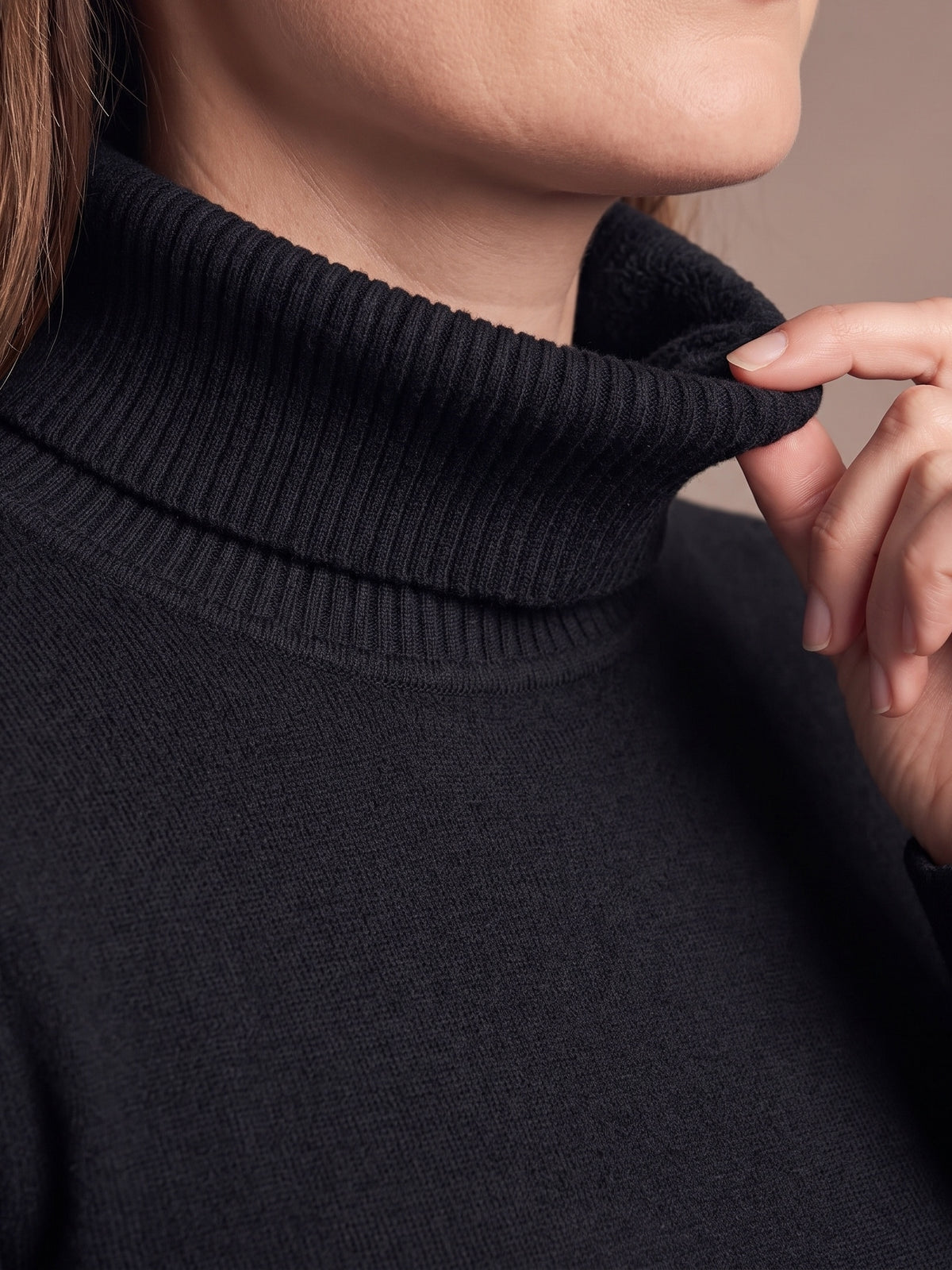 Close-up of the fold-over ribbed collar of the black plush-lined turtleneck worn on the neck, fingers lifting the folded edge