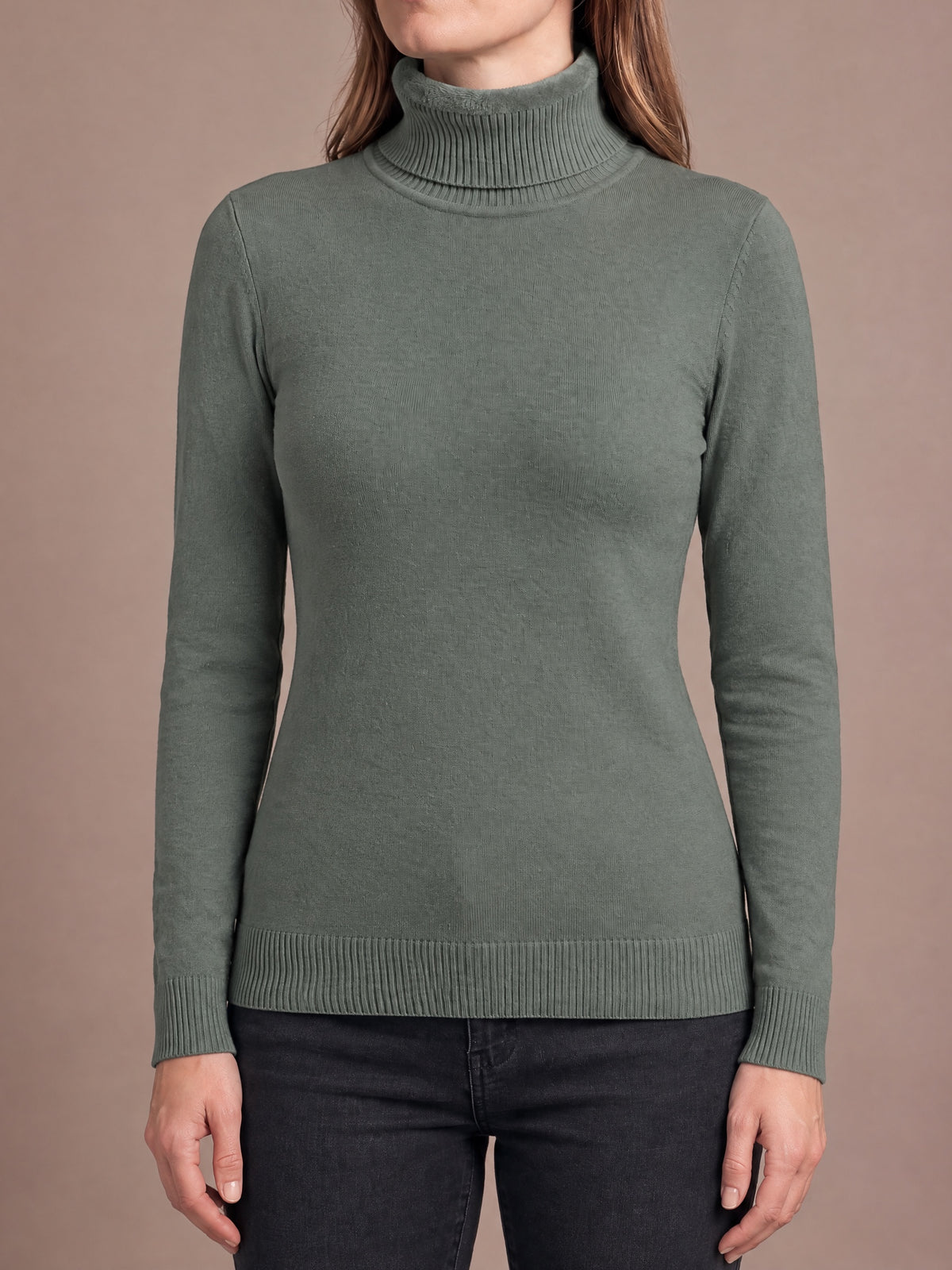 Woman wearing the plush-lined knit turtleneck in grey green, standing square-on with arms relaxed, fold-over collar with plush inside, ribbed cuffs and hem
