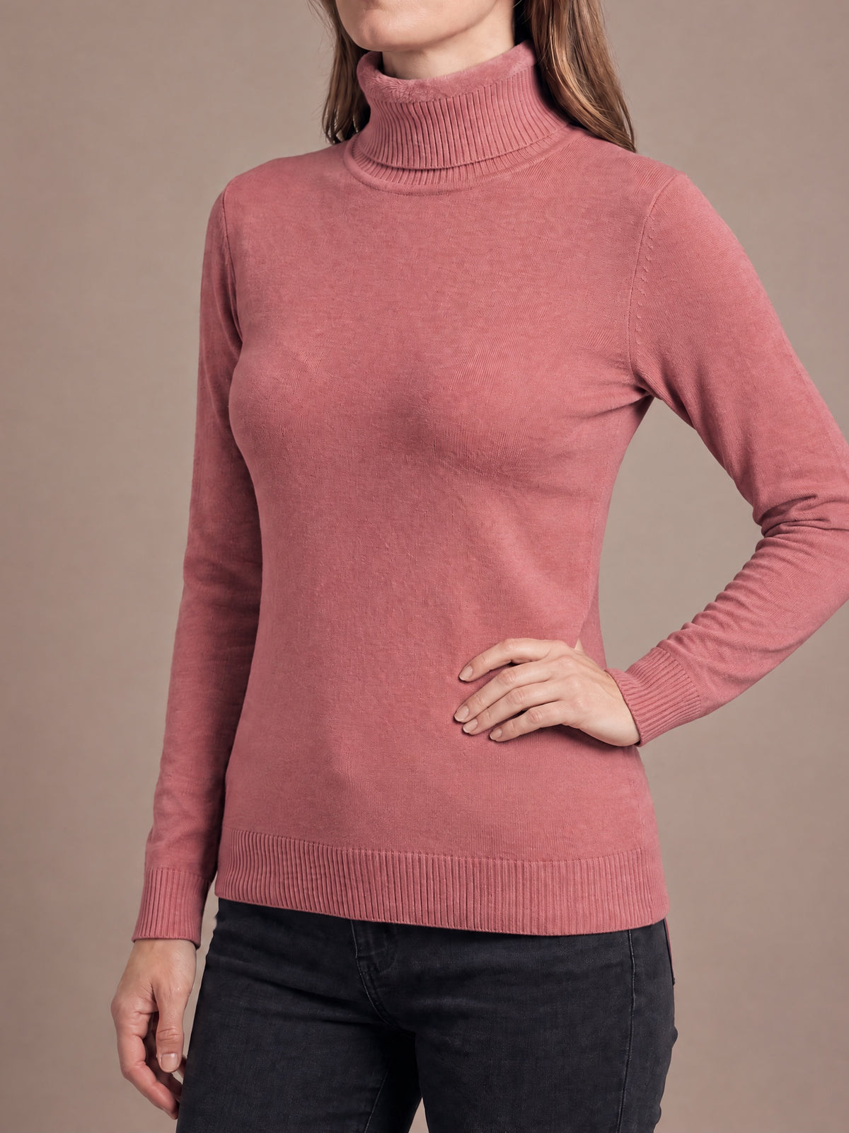 Woman wearing the plush-lined knit turtleneck in rose red with one hand on the hip, fold-over collar, slim fit and ribbed cuffs and hem