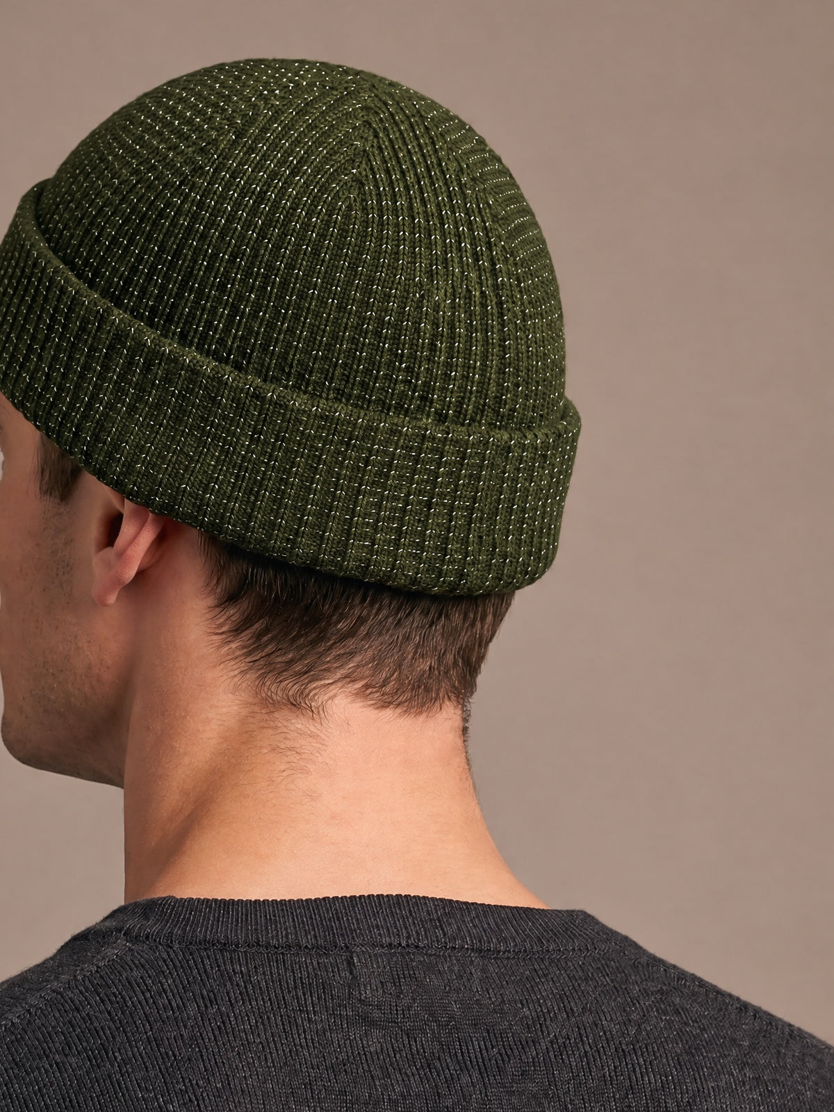 Reflective rib-knit beanie in green worn by a man seen from behind with the chin slightly raised, short crown, folded cuff and reflective flecks