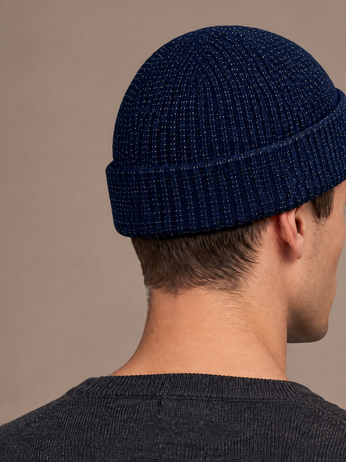 Reflective rib-knit beanie in navy worn by a man seen from the right side-back, short crown, folded cuff and reflective flecks in the knit