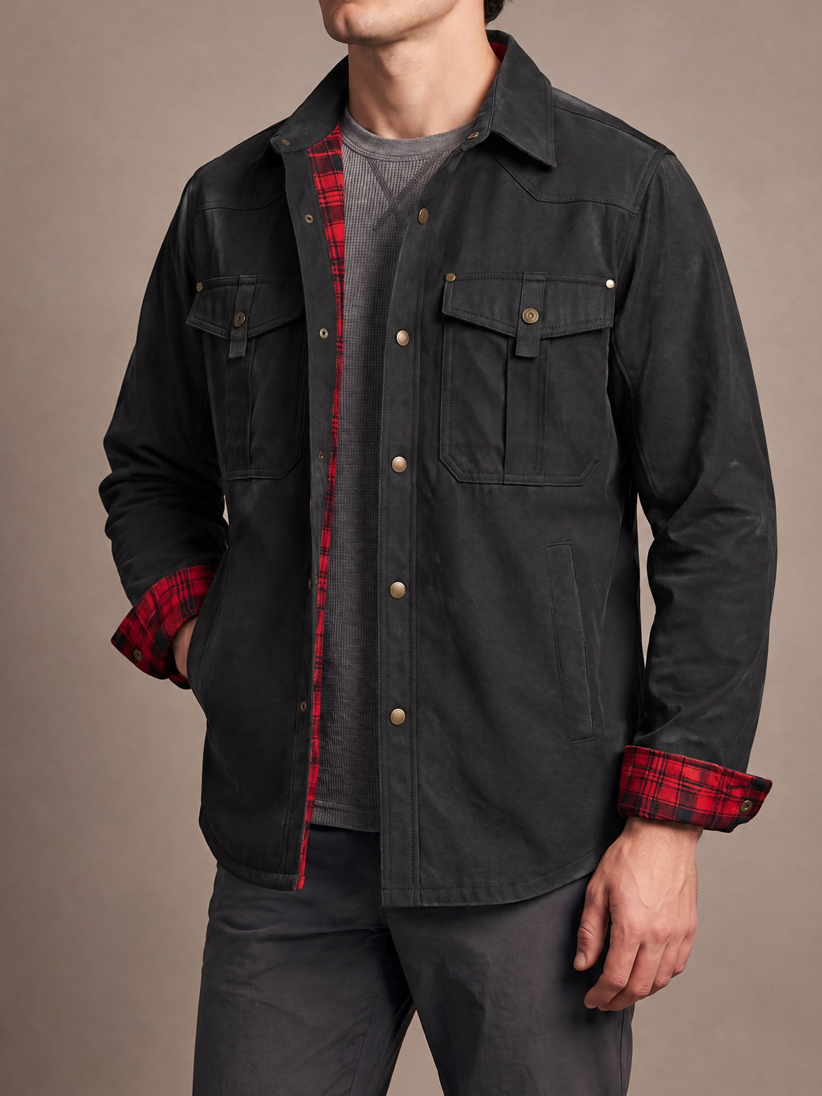 Flannel-lined shirt jacket in black with red plaid lining and cuffs, worn open with a hand in the side pocket