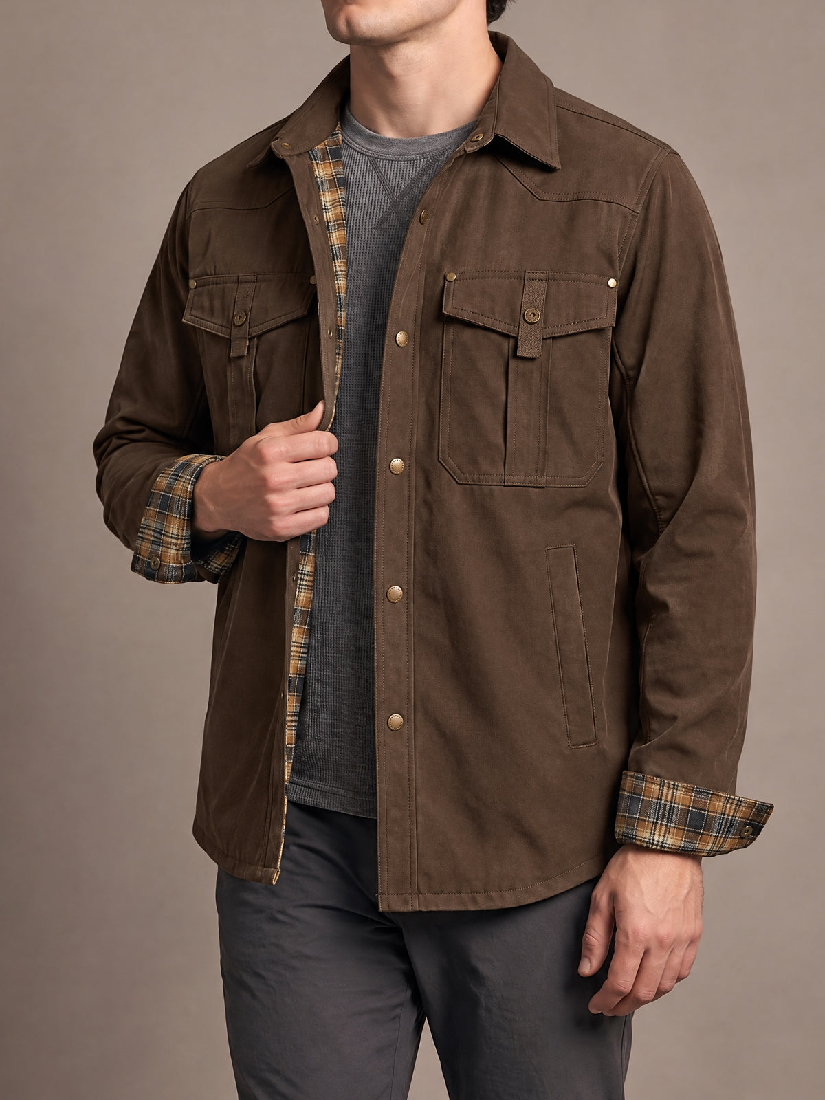 Flannel-lined shirt jacket in dark brown with brown and mustard plaid lining and cuffs, one hand at the front edge