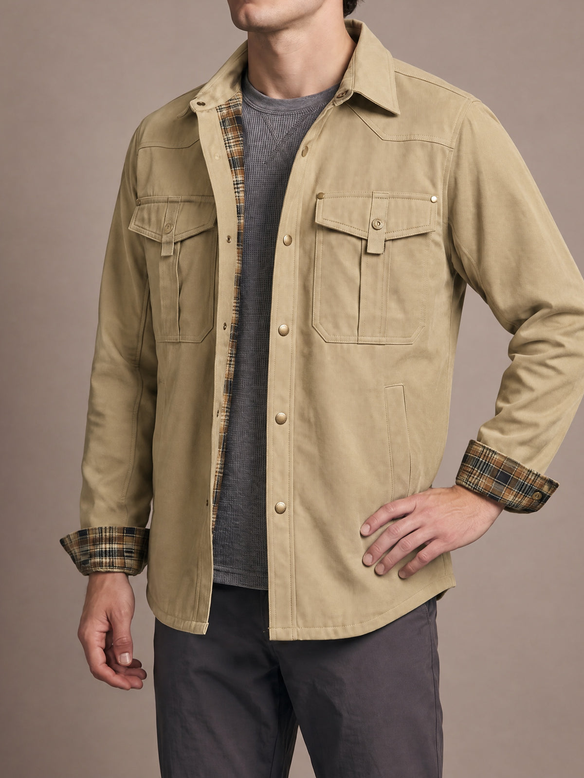Flannel-lined shirt jacket in khaki with brown plaid lining and cuffs, worn open with one hand on the hip
