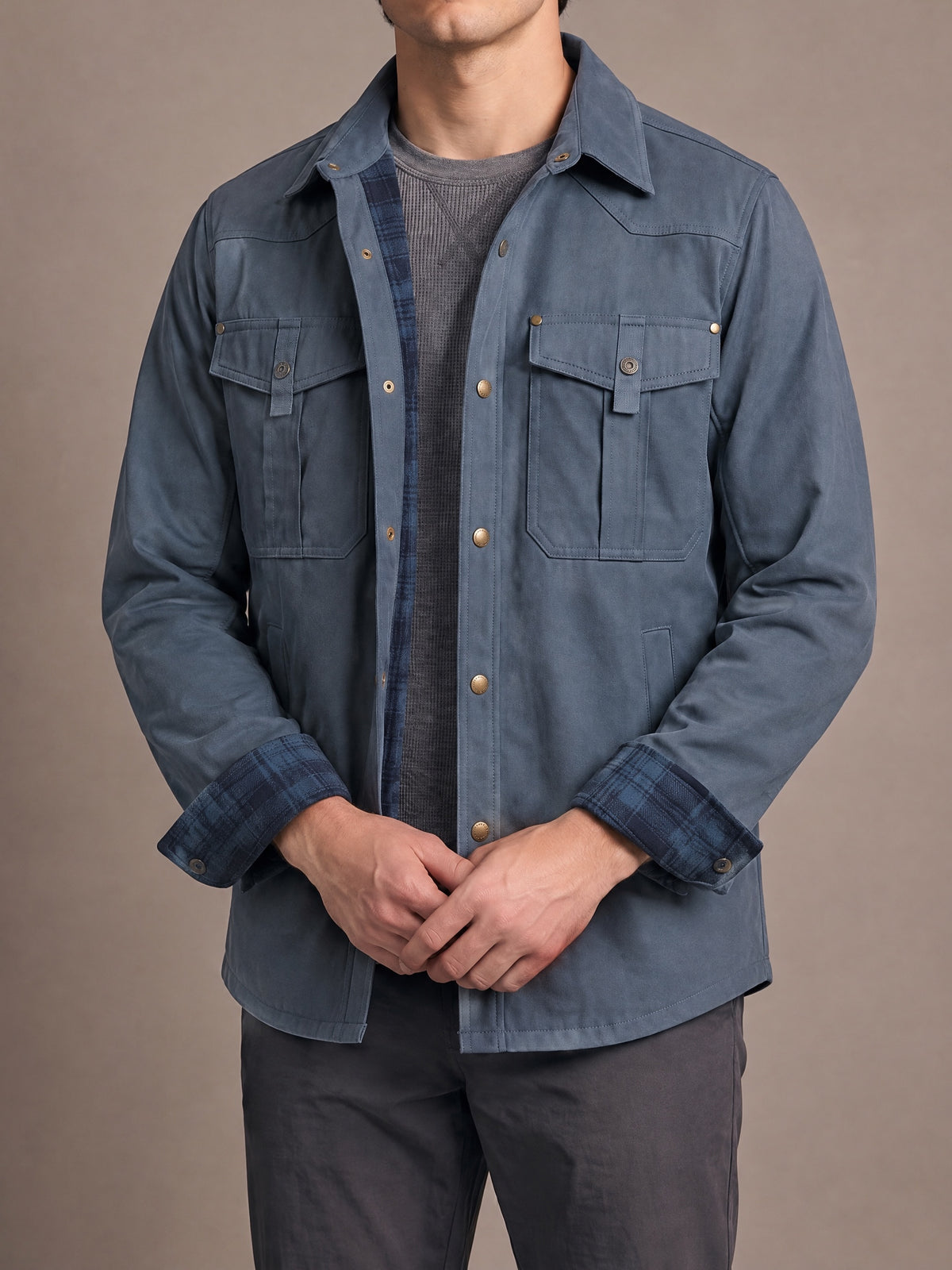 Flannel-lined shirt jacket in slate blue with navy plaid lining and cuffs, worn open with hands clasped in front