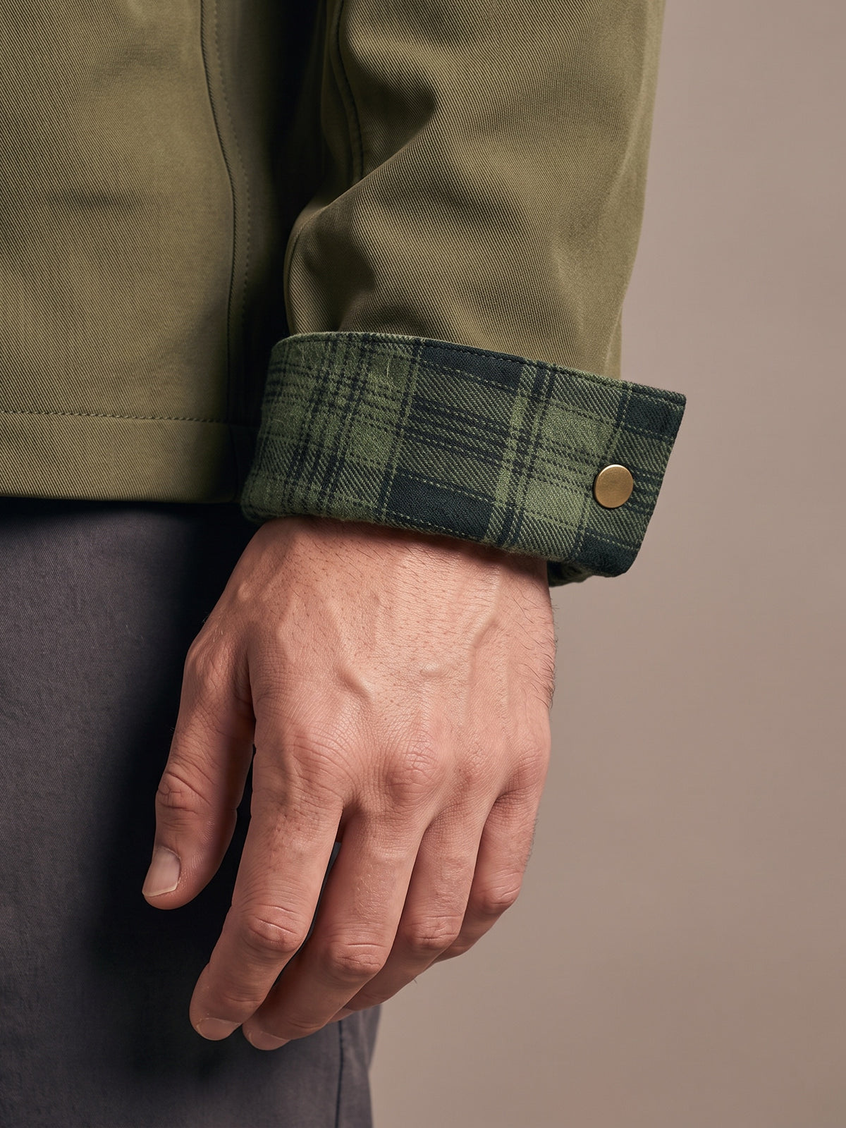 Flannel-lined cuff turned back once on the army green shirt jacket, green plaid inside and a brass snap