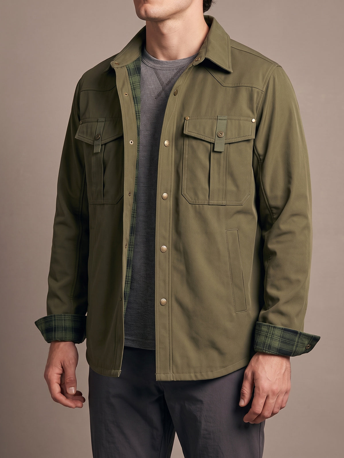 Army green flannel-lined shirt jacket worn open over a grey base layer, two snap-flap chest pockets, slit hand pockets and plaid cuffs turned back
