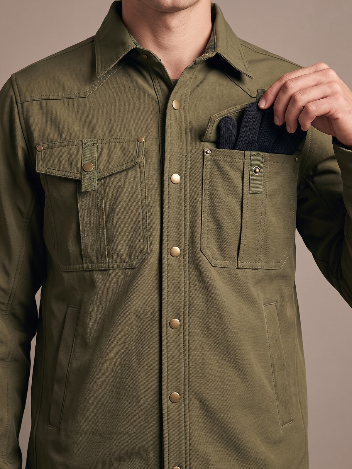 Two snap-flap chest pockets on the army green shirt jacket, one flap lifted with knit gloves tucked inside