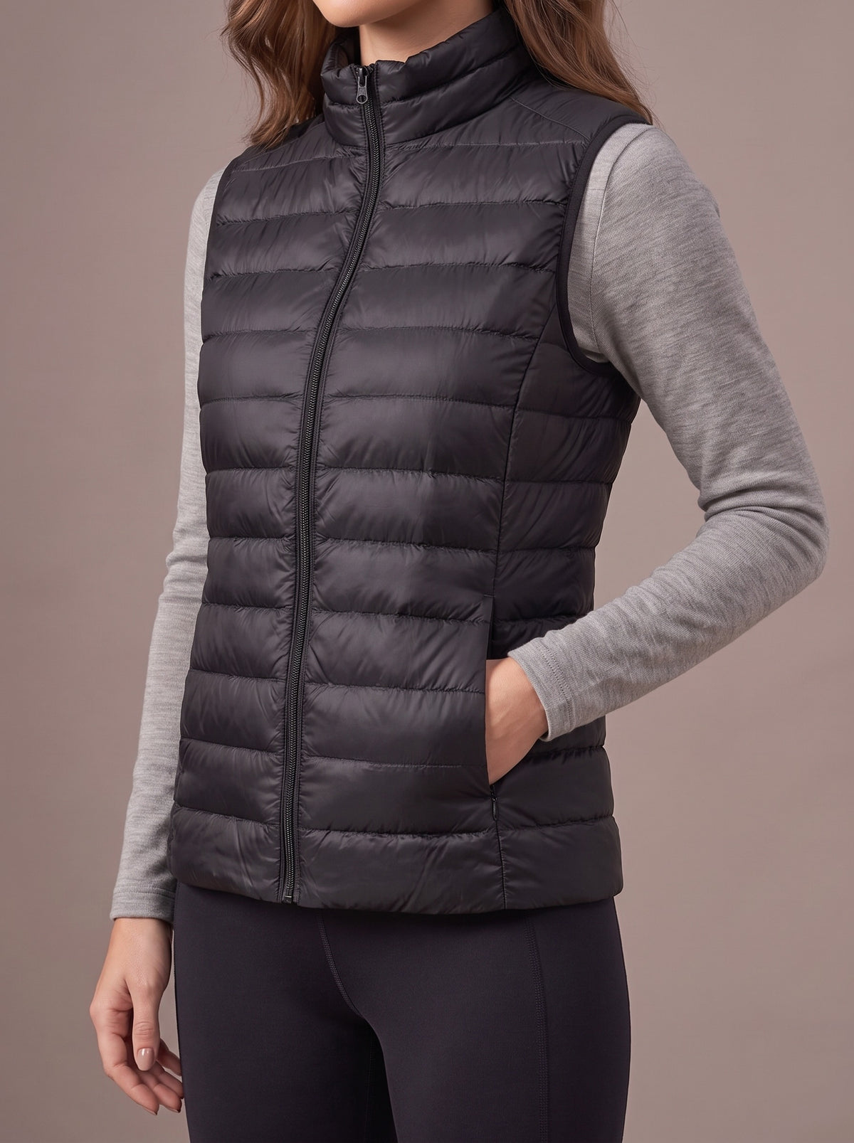Black packable down vest with low stand-up collar over a grey top, studio view