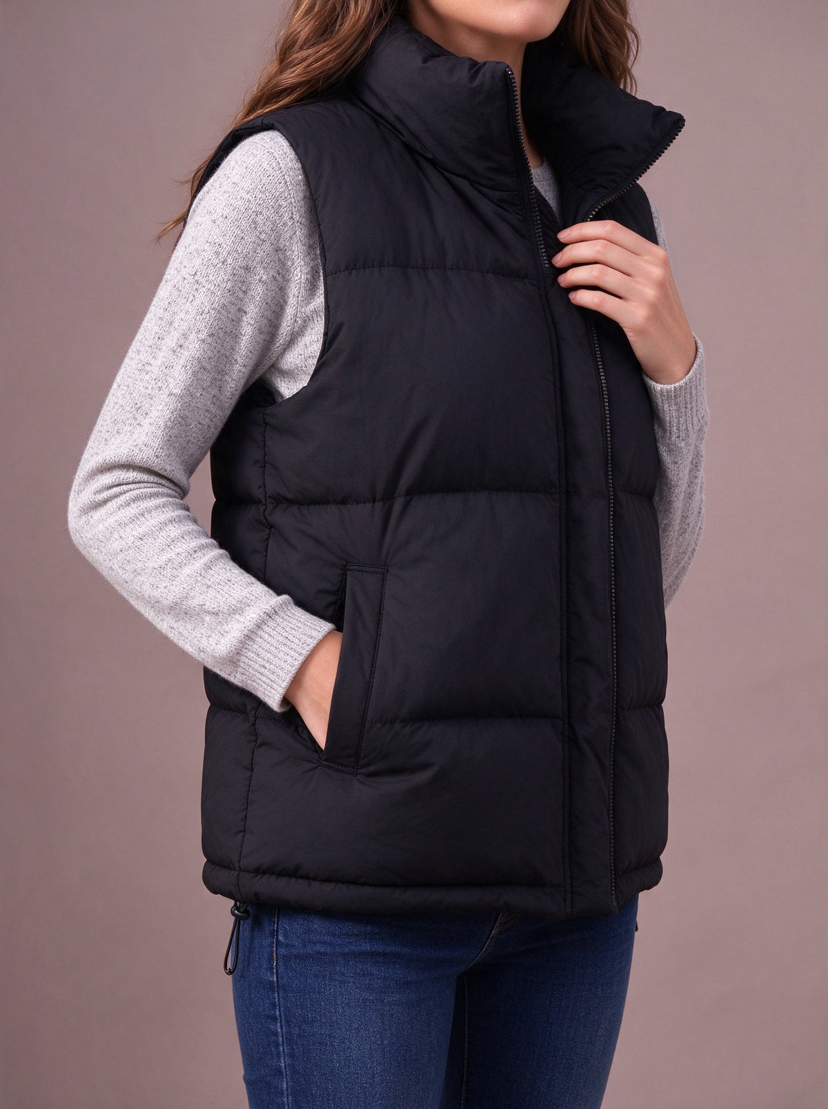 Black quilted vest over a grey knit, hand in a pocket, studio view