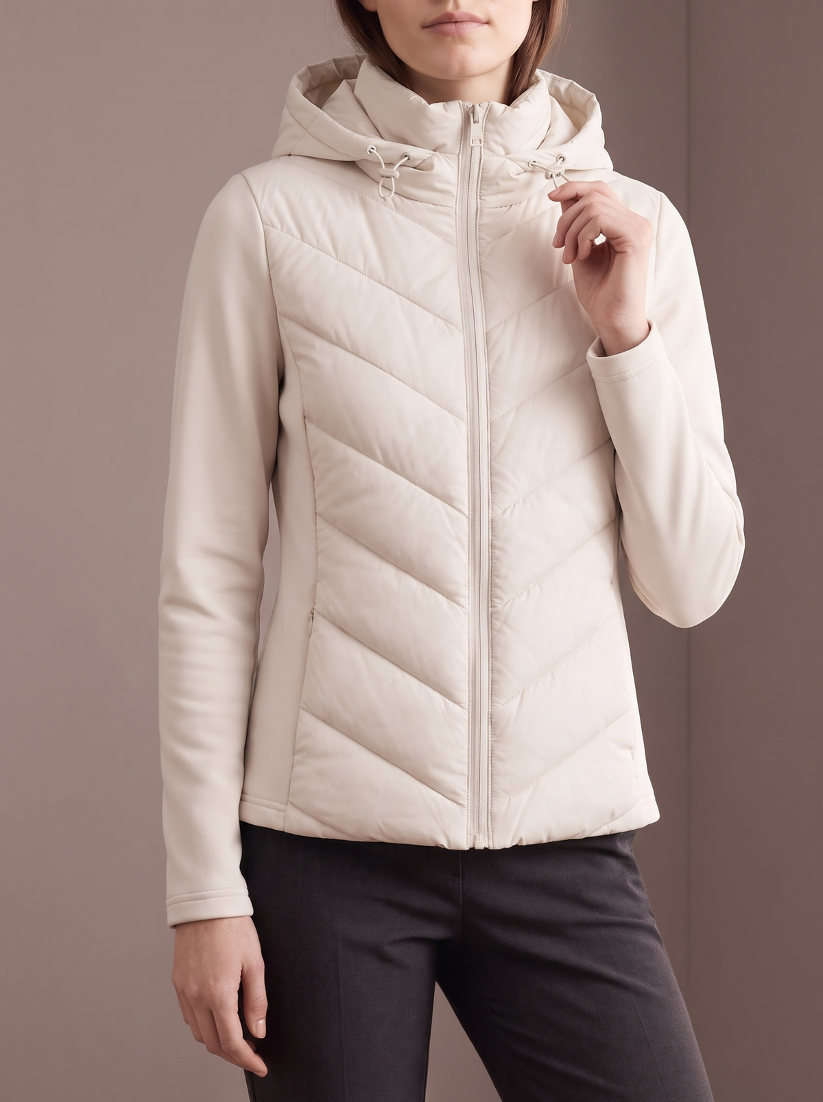 Women's beige chevron hybrid jacket, hand at the hood drawcord, studio front view