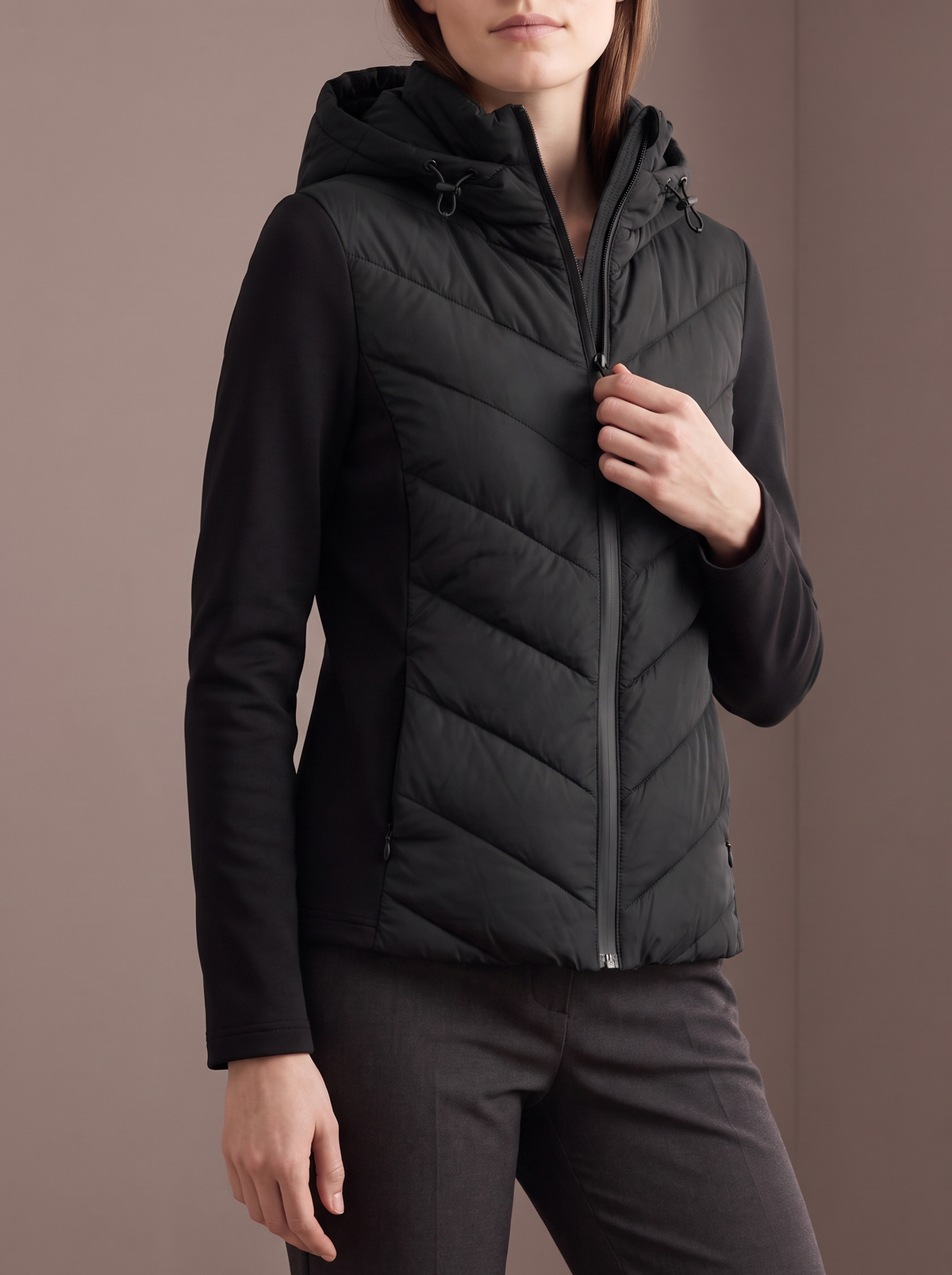 Women's black chevron hybrid jacket, hand on the zip, studio view