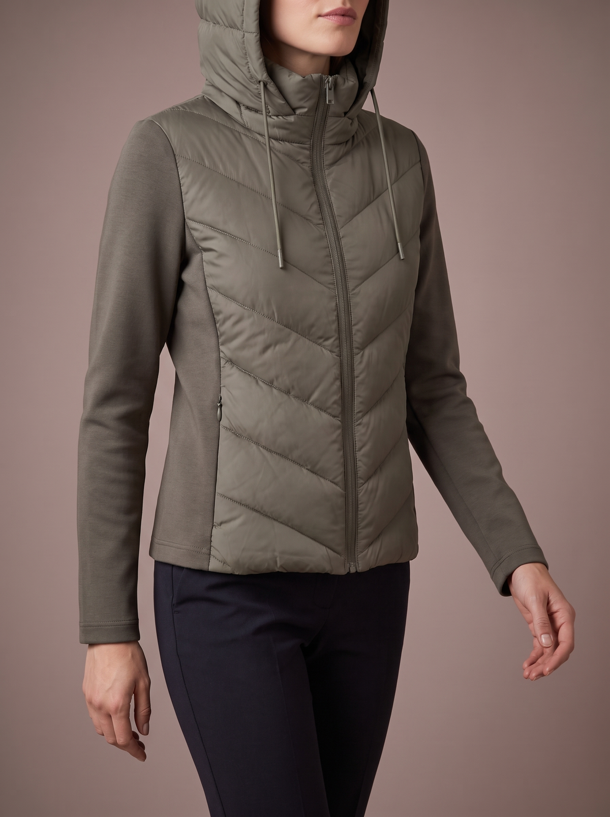 Women's olive green chevron hybrid jacket with the hood up, mid-step in the studio