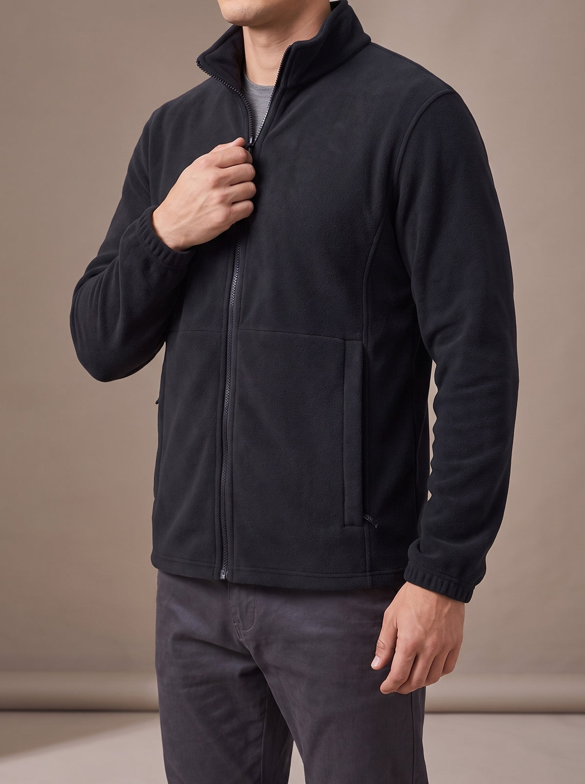 Man pulling up the zip of the black polar fleece jacket, studio three-quarter view