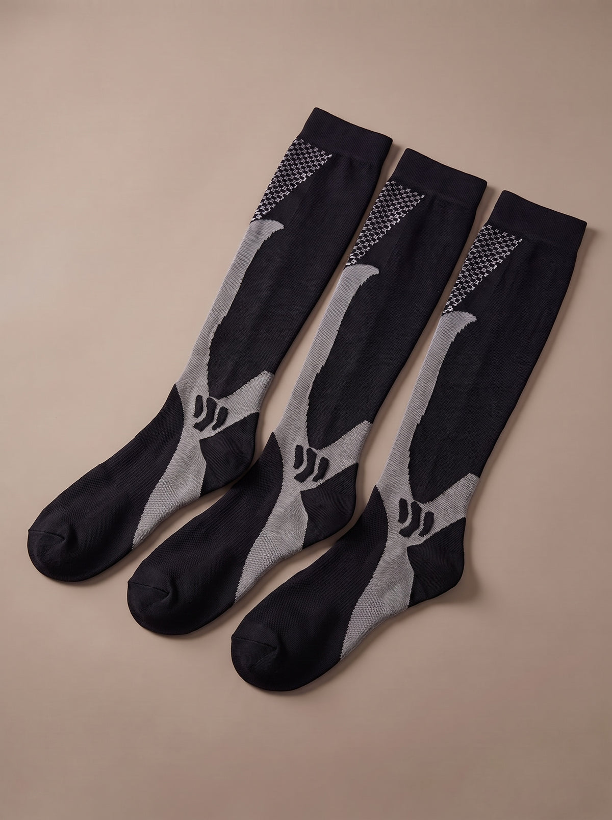 Three black knee-high compression socks with grey stripe, grey ankle zone and checker panel, fanned out, studio view