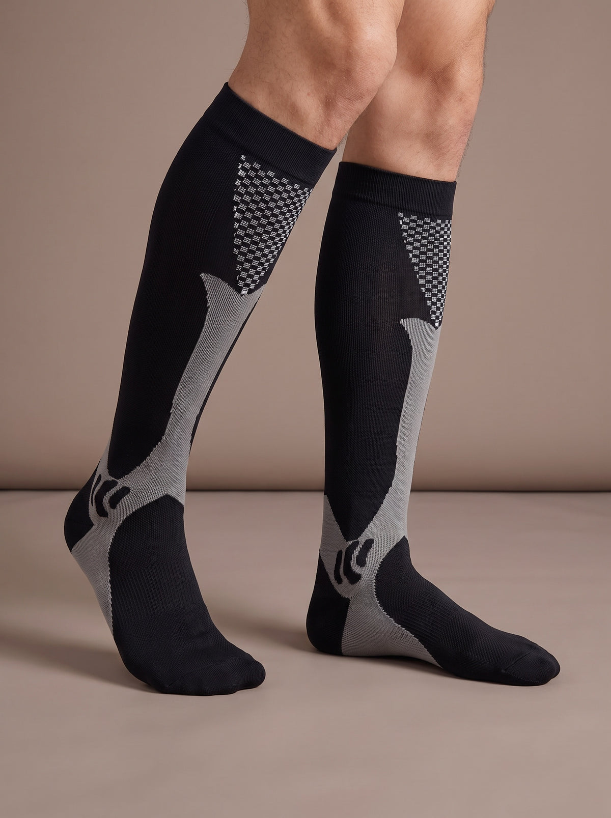 Lower legs in black knee-high compression socks with grey stripe and checker panel, studio view cropped at the knee
