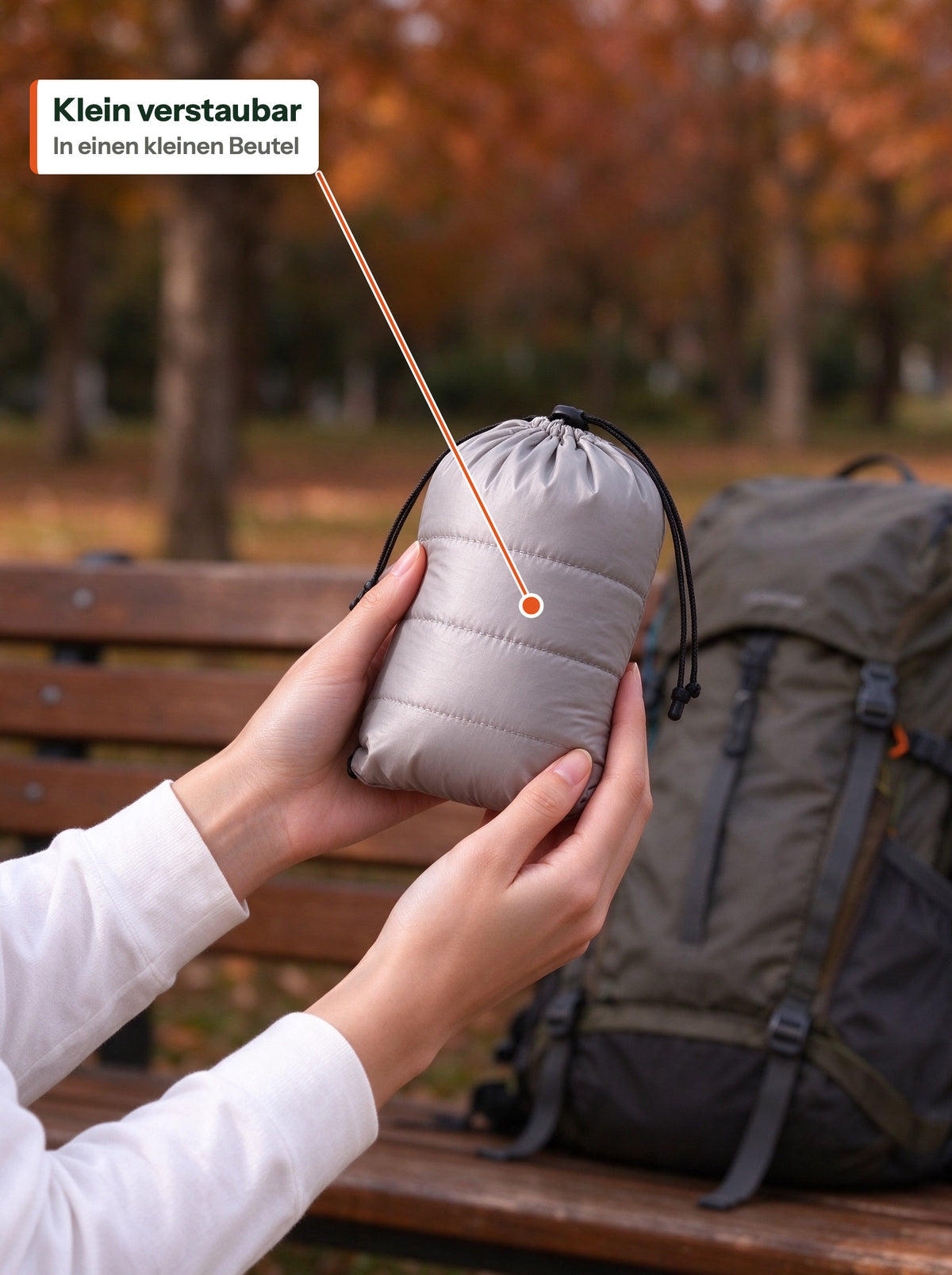 Light down jacket packed into a small stuff bag, held in two hands (DE Label)