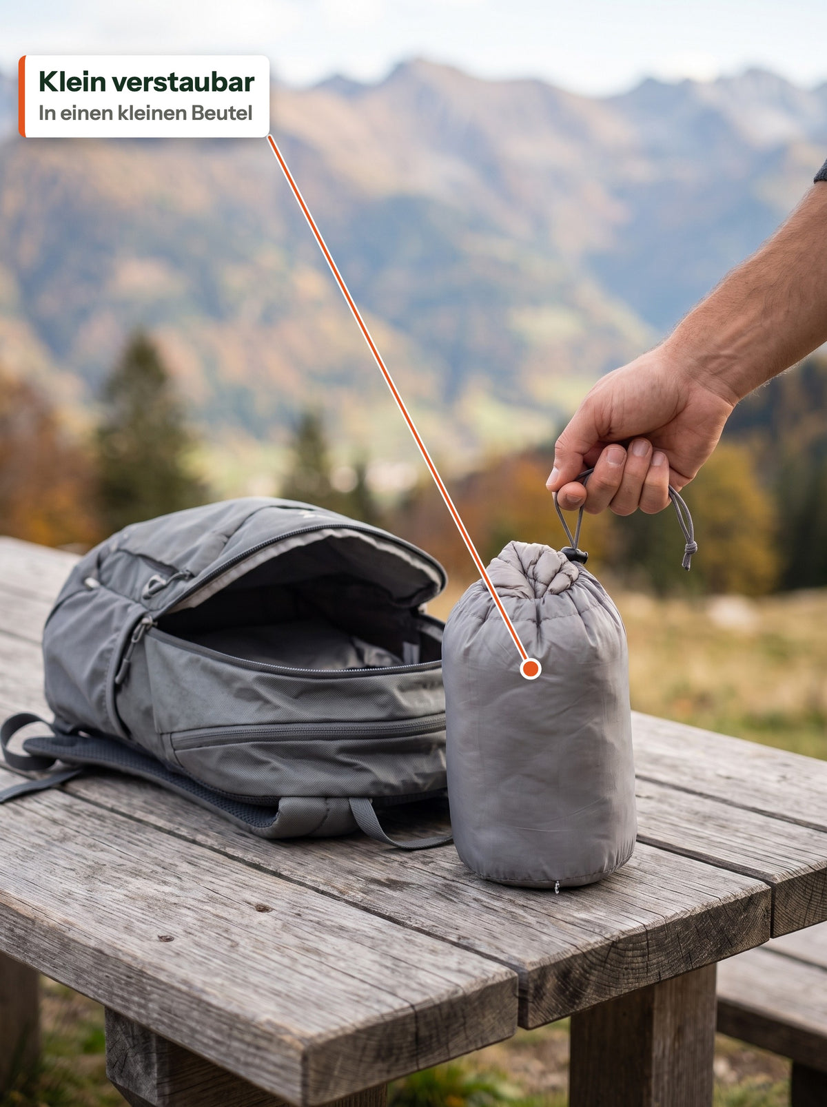 Daunenjacke in einem kleinen Packbeutel neben einem Tagesrucksack (DE label)