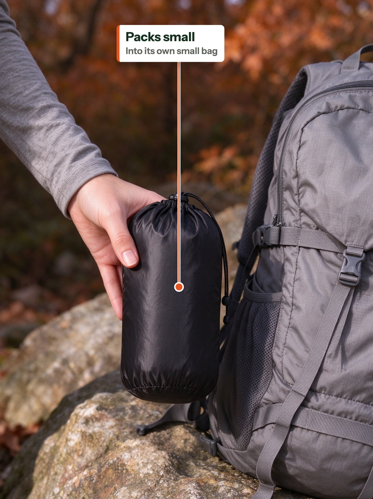 Down vest packed into a small black stuff bag next to a backpack (EN label)