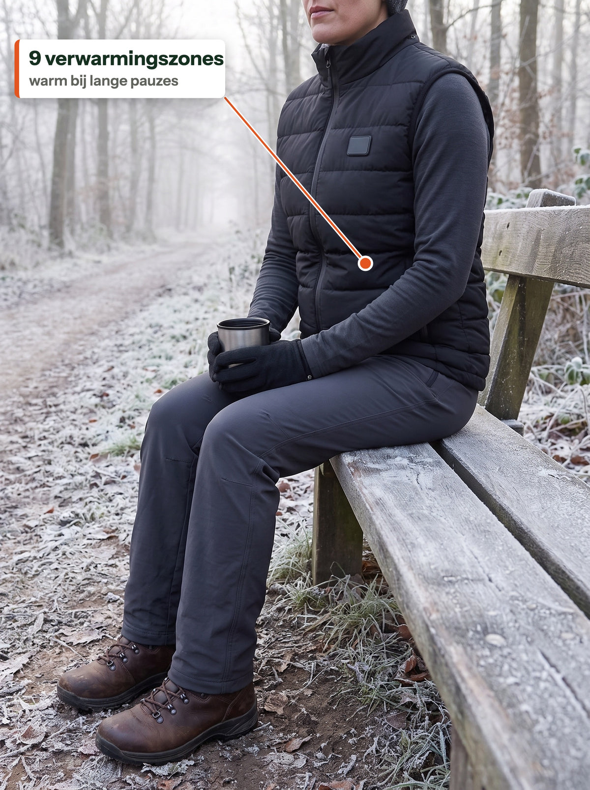 Vrouw in de zwarte HeatCore Bodywarmer op een bankje langs een berijpt wandelpad met warme drank: 9 verwarmingszones, warm bij lange pauzes