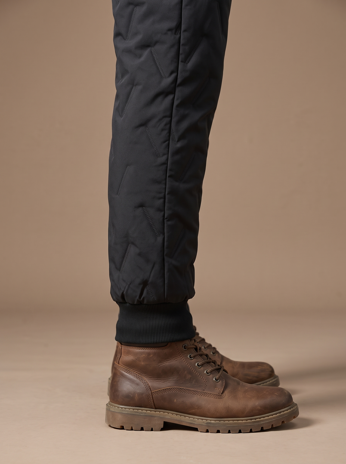 Ribbed ankle cuff of the black quilted trouser closing over the top of a brown leather walking boot