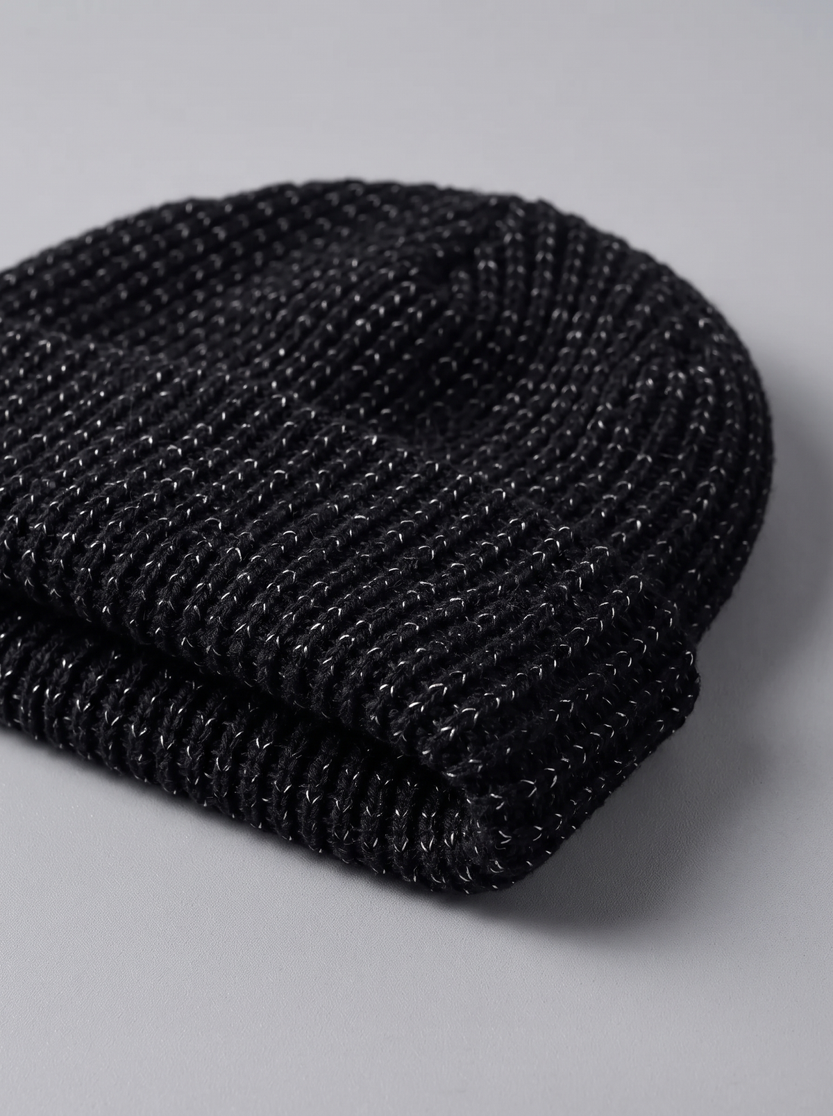 Close-up of the folded cuff and short rib-knit crown of the black reflective beanie