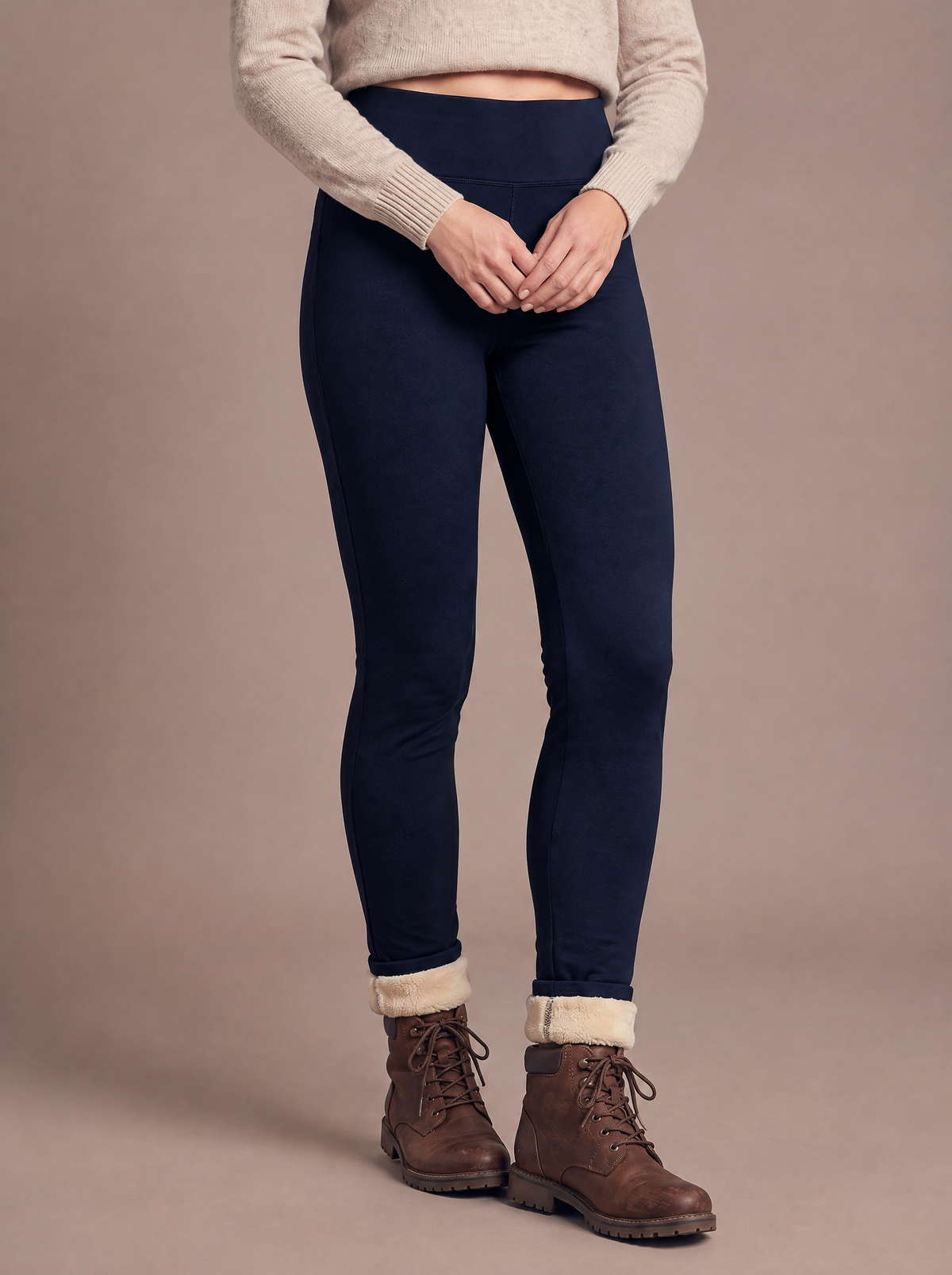 Woman wearing the high-waist sherpa-lined legging in navy, a half step forward with hands clasped at the waistband, cream lining at the turned-up ankles above brown walking boots