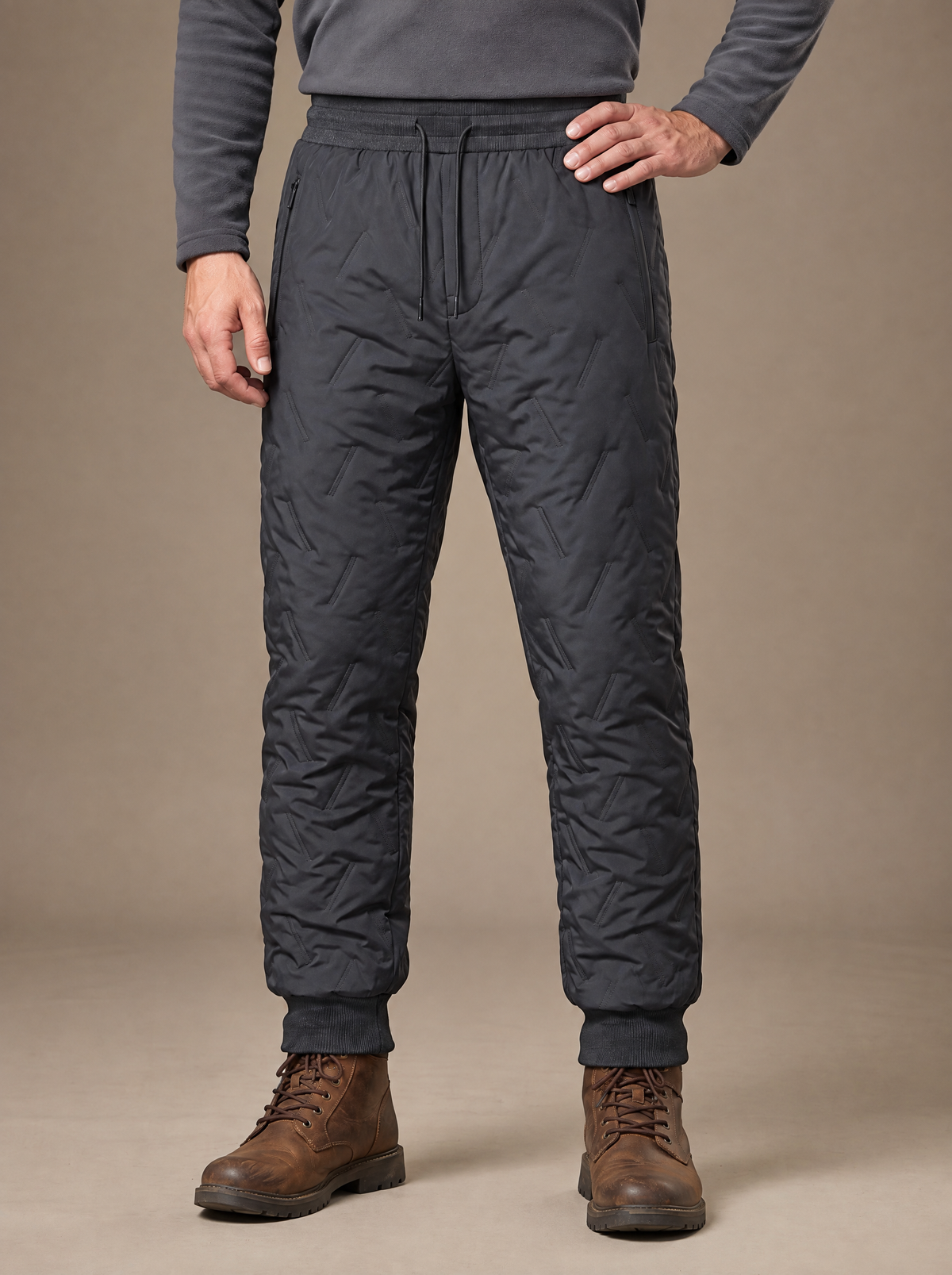 Man wearing the wave-quilted sherpa-lined trouser in charcoal grey, standing square-on with one hand on the hip, drawcord waist, zip side pocket and ribbed ankle cuffs over brown walking boots