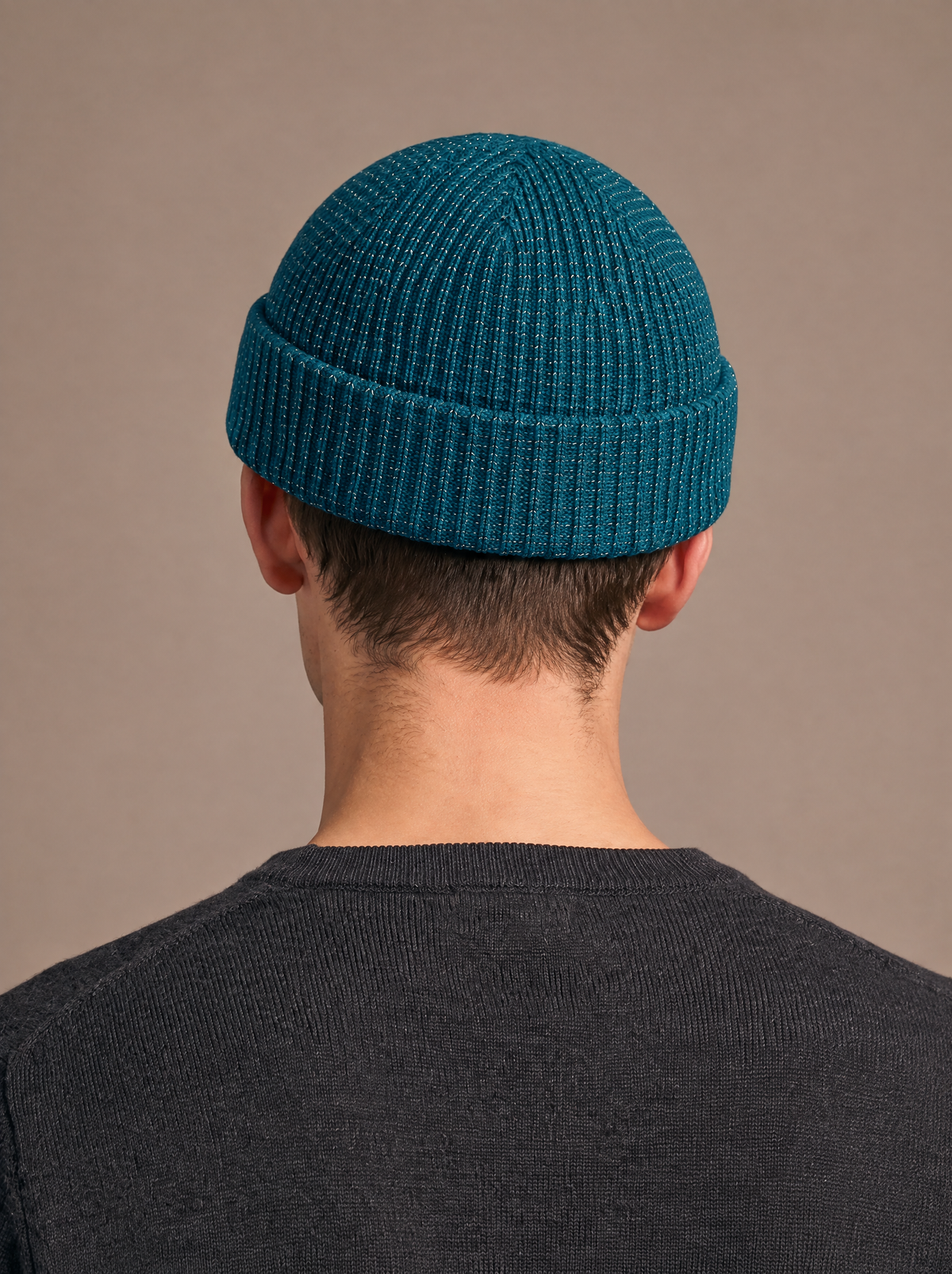 Reflective rib-knit beanie in teal worn by a man seen straight from behind, short crown, folded cuff and reflective flecks in the knit