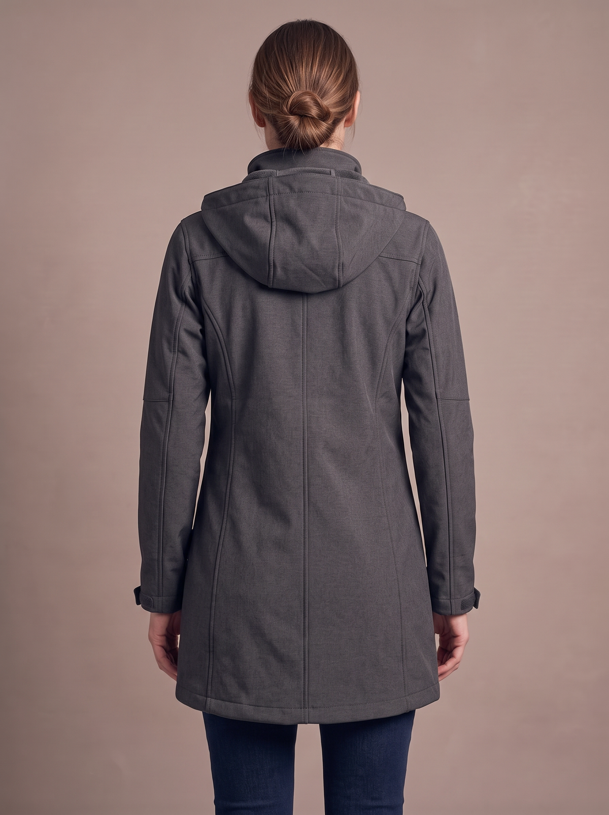 Back view of the charcoal softshell coat worn, hood down, hem at mid-thigh covering the seat, back panel seams and cuff tabs