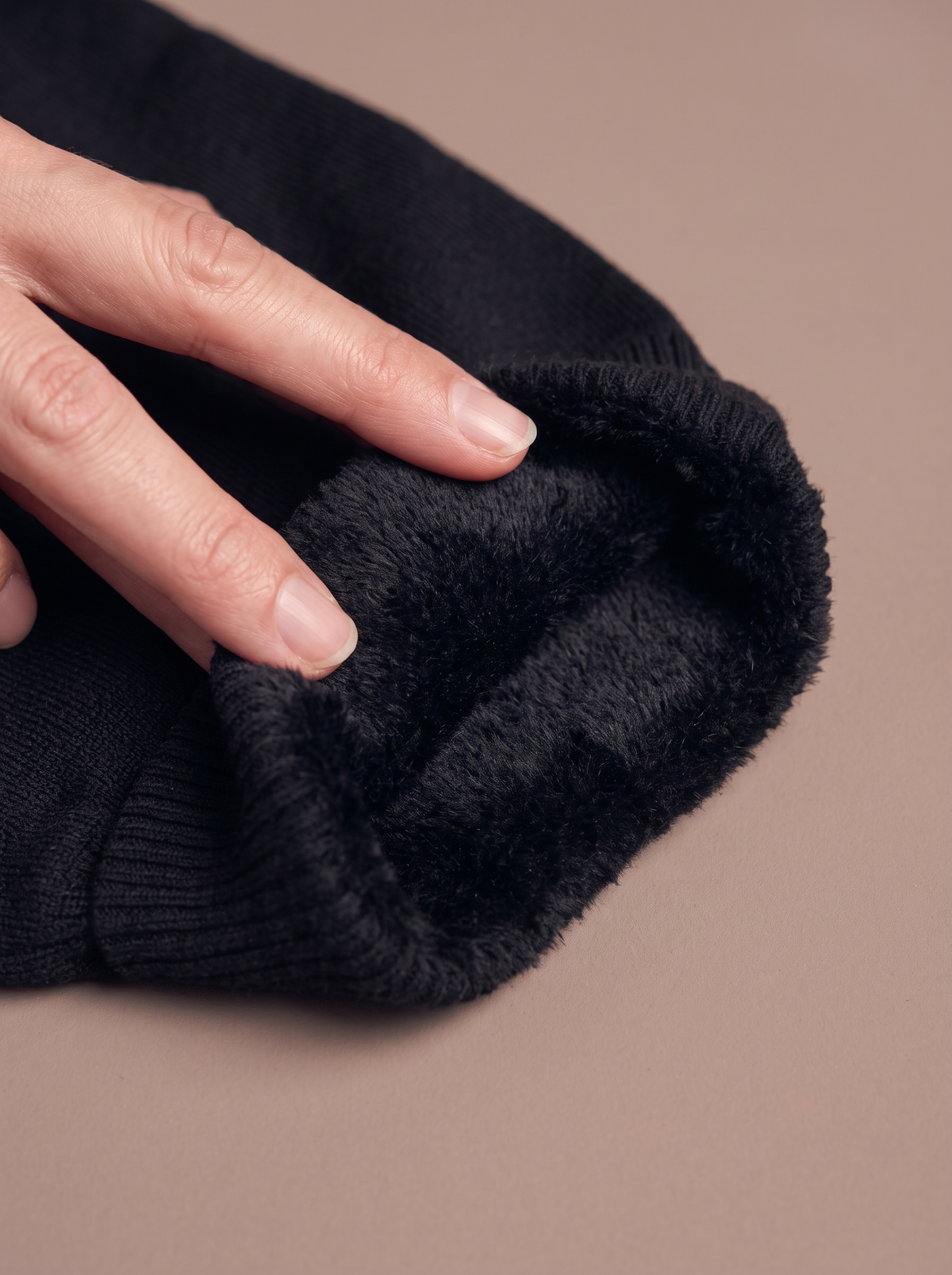 Macro of the black fine rib knit folded back by a hand to show the deep, soft black plush lining