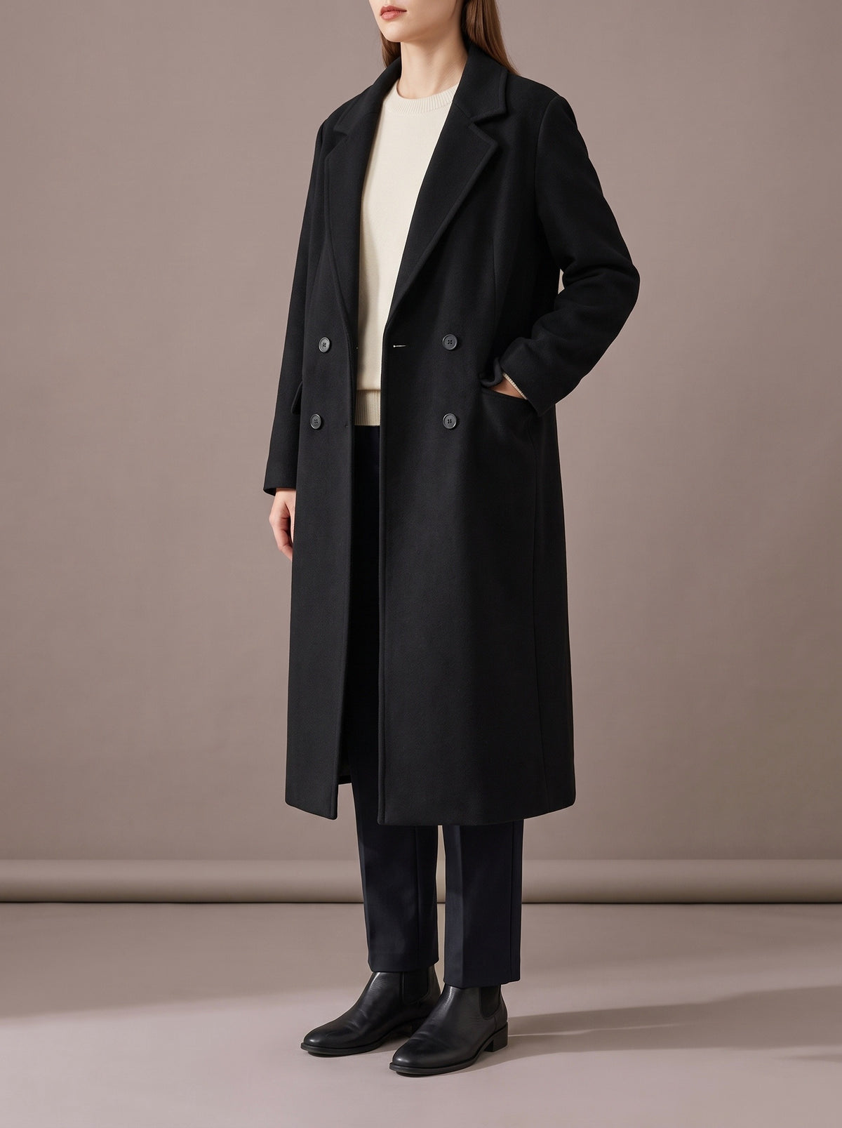 Woman in the black long double-breasted coat with notched lapels, hand in the flap pocket, studio view