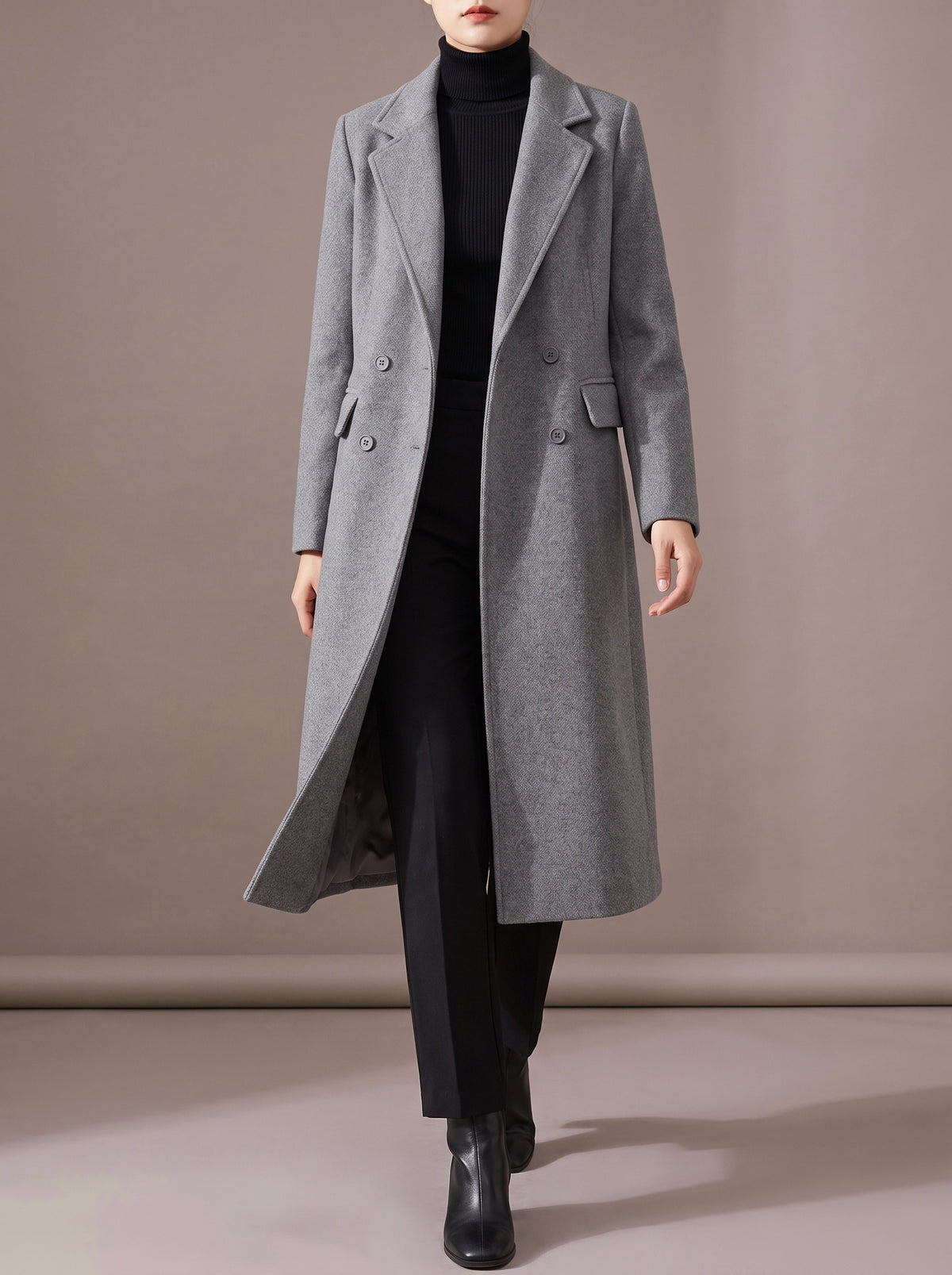 Woman walking in the grey long double-breasted coat worn open over a black turtleneck, studio view