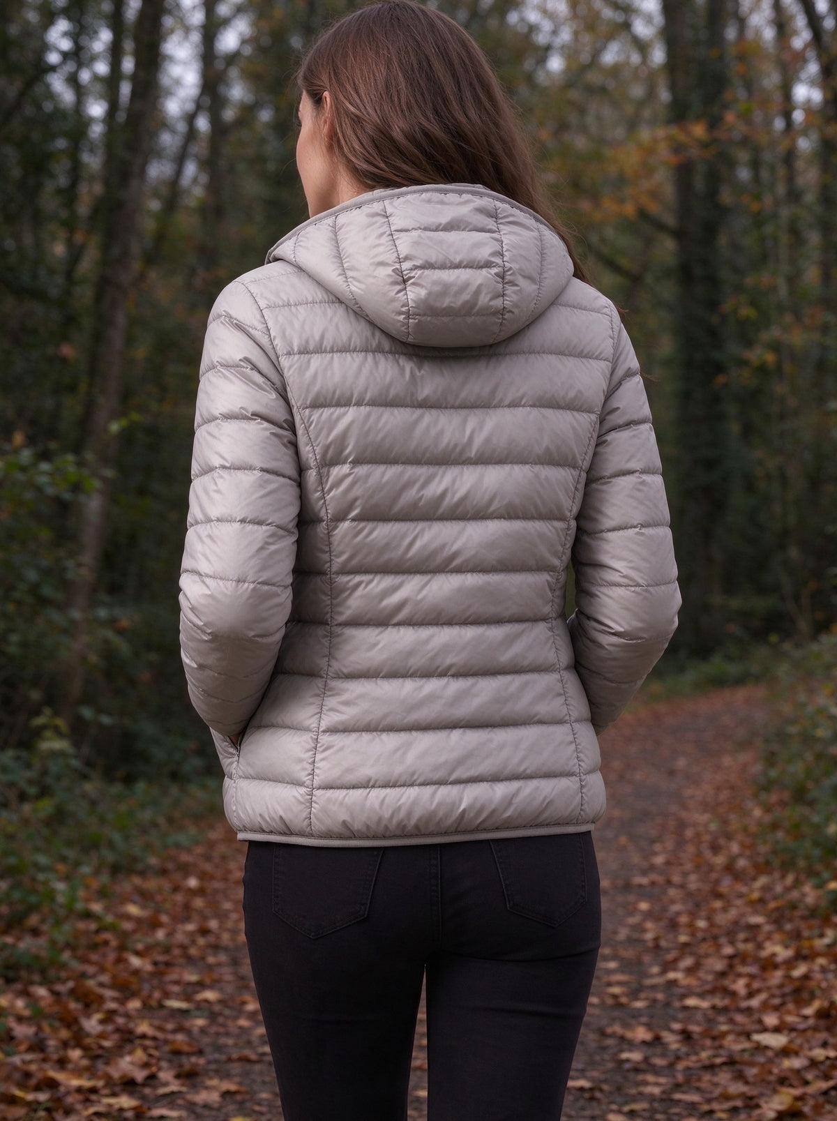 Woman in the grey light down jacket walking on a forest path in autumn