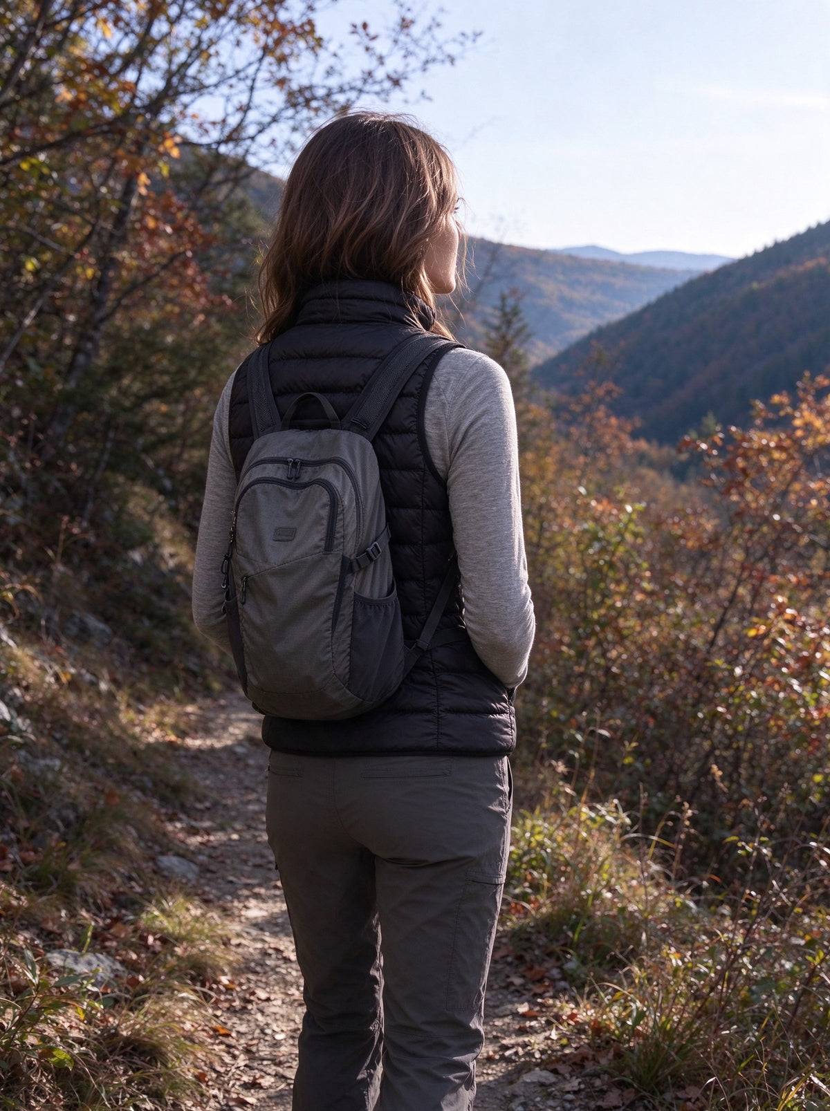 Woman in the black packable down vest on a mountain trail on a cold autumn morning