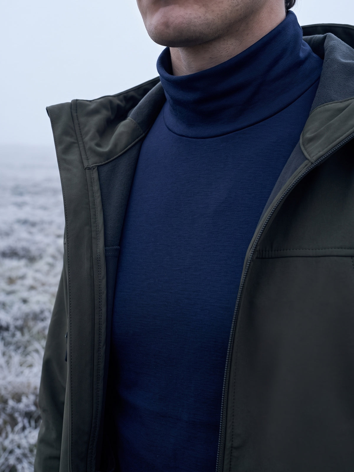 Navy mock neck base layer with its folded collar up to the jaw, closing the gap under an open jacket on a frosty morning